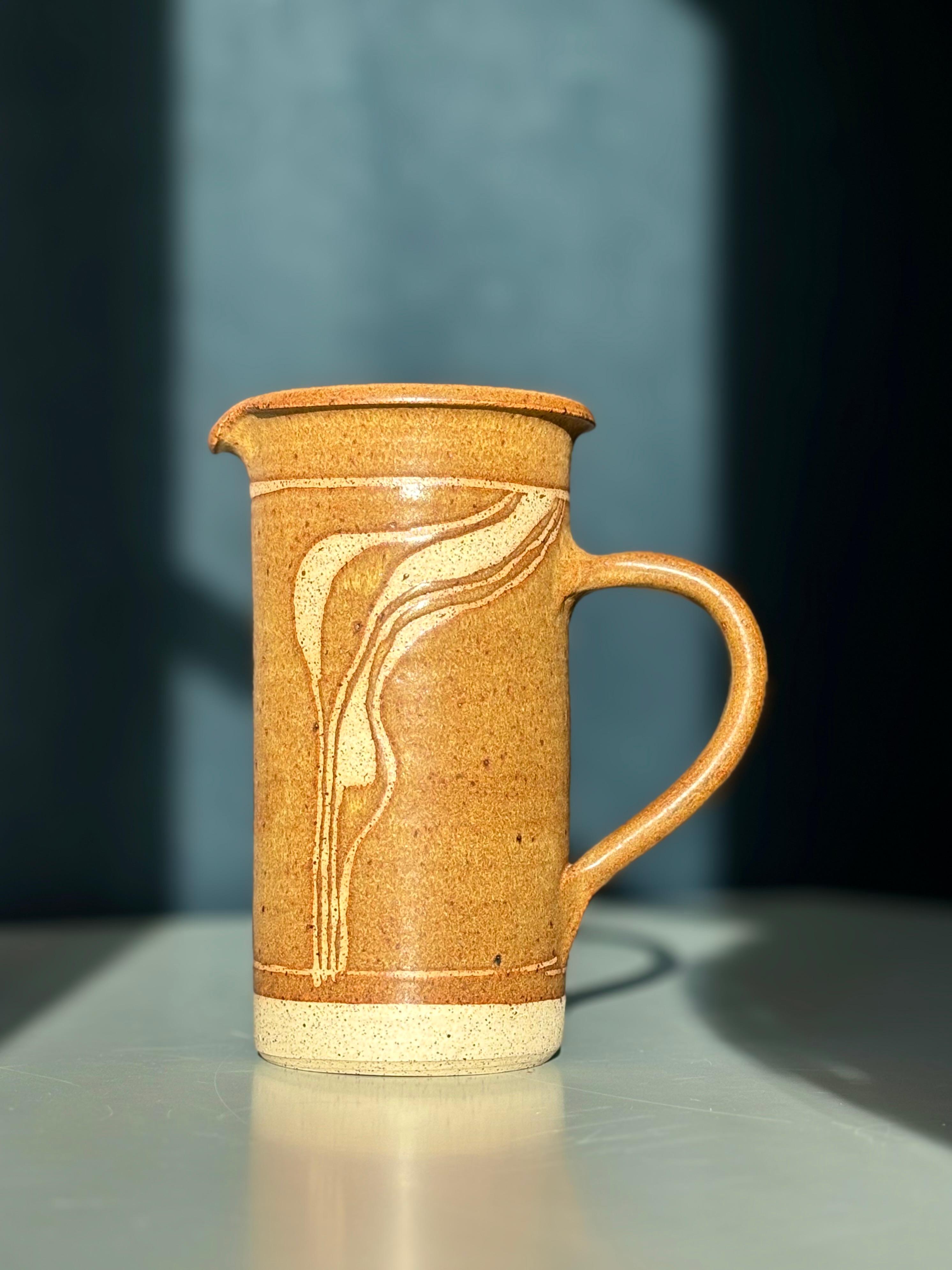Pichet en grès fabriqué à la main par Ulsnes Keramik sur la petite île danoise de Langeland dans les années 1980. Émail chaud brun caramel avec motif organique tourbillonnant sculpté à la main sur une face exposant le matériau céramique non émaillé.