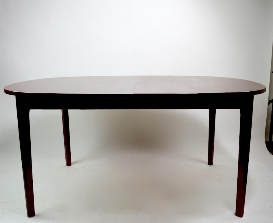 Sophisticated Danish modern dining table in rosewood with one hidden leaf. This table is in good original condition, showing only light cosmetic wear, normal and consistent with age. Total length with leaf in place 84.75 inches w/o leaf 61.25