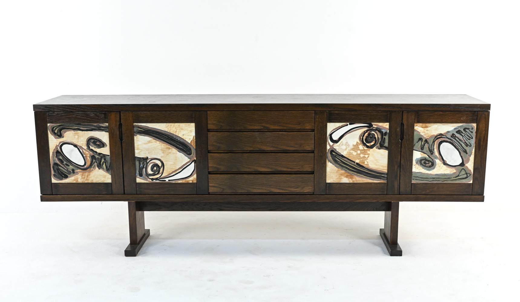 A fabulous Danish modern sideboard in rich, dark stained oak veneer with a sturdy trestle base. Central drawers with integral recessed handles are flanked by two sets of cabinet doors, inset with stunning Ox Art organic-inspired abstract design