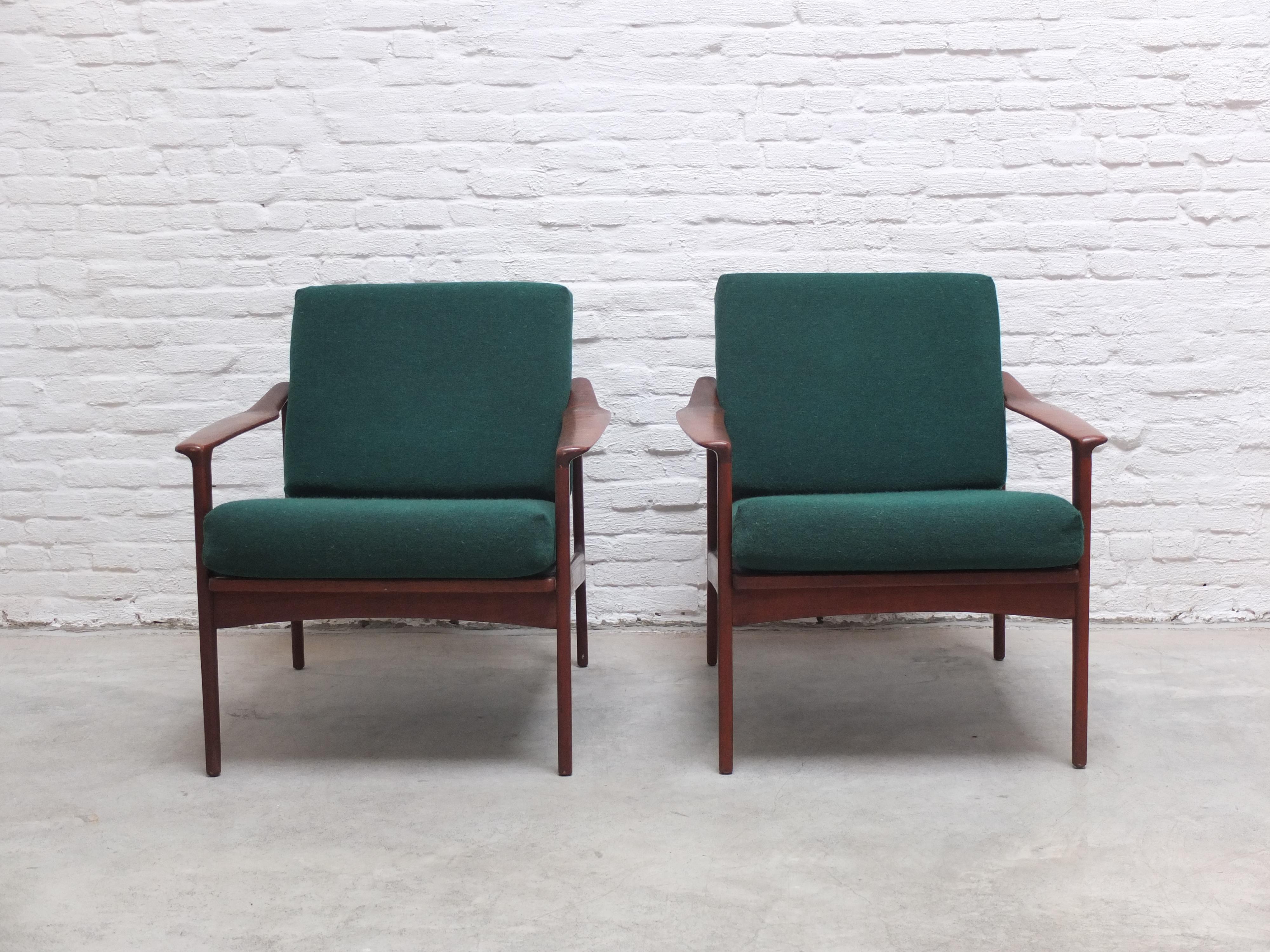 Lovely pair of easy chairs designed by Ib-Kofod Larsen for Selig during the 1960s. These elegant chairs have solid teak frames with beautiful sculptural armrests and brass joints. The forest green cushions have been refilled with new foam. In very