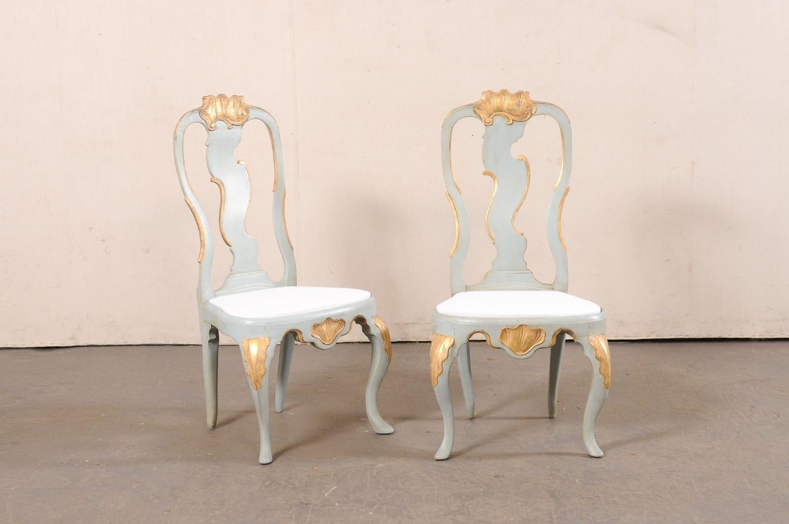 A Danish pair of period Rococo painted and carved-wood side chairs, with upholstered seats, from the 18th century. These antique chairs from Denmark have been created in typical Rococo fashion with beautiful asymmetrical carvings about their top