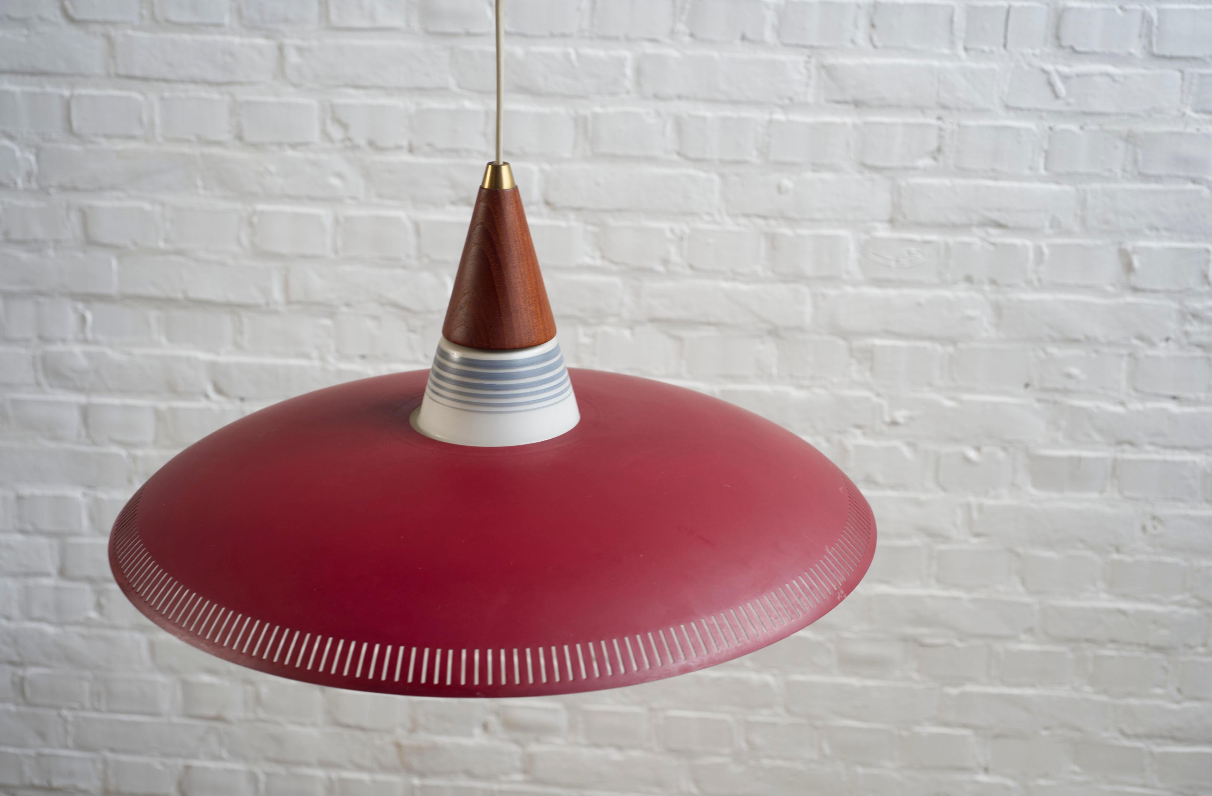 Una bellissima lampada a sospensione danese che ricorda gli am designs di Bent Karbly per Lyfa, anni '60.

Un paralume in metallo bordeaux si appoggia su un paralume interno in vetro opalino. Lampada molto elegante con un piano in teak tornito con