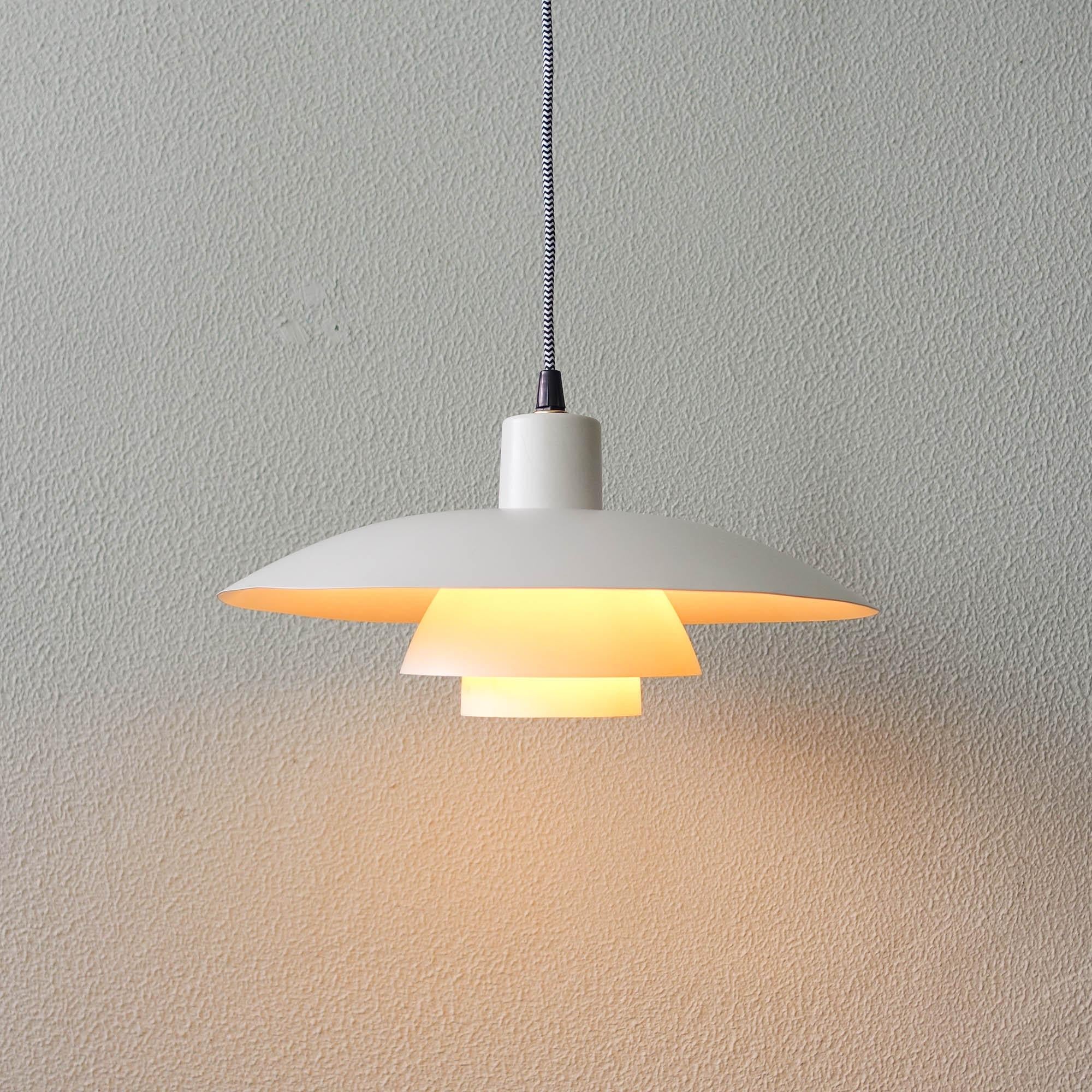 This pendant was designed by Poul Henningsen and produced by Louis Poulsen, in Denmark during the 1960s. It is made of powder-coated aluminum and is lit both downwards and from the sides. The PH 4/3 model is based on the principle of a reflecting