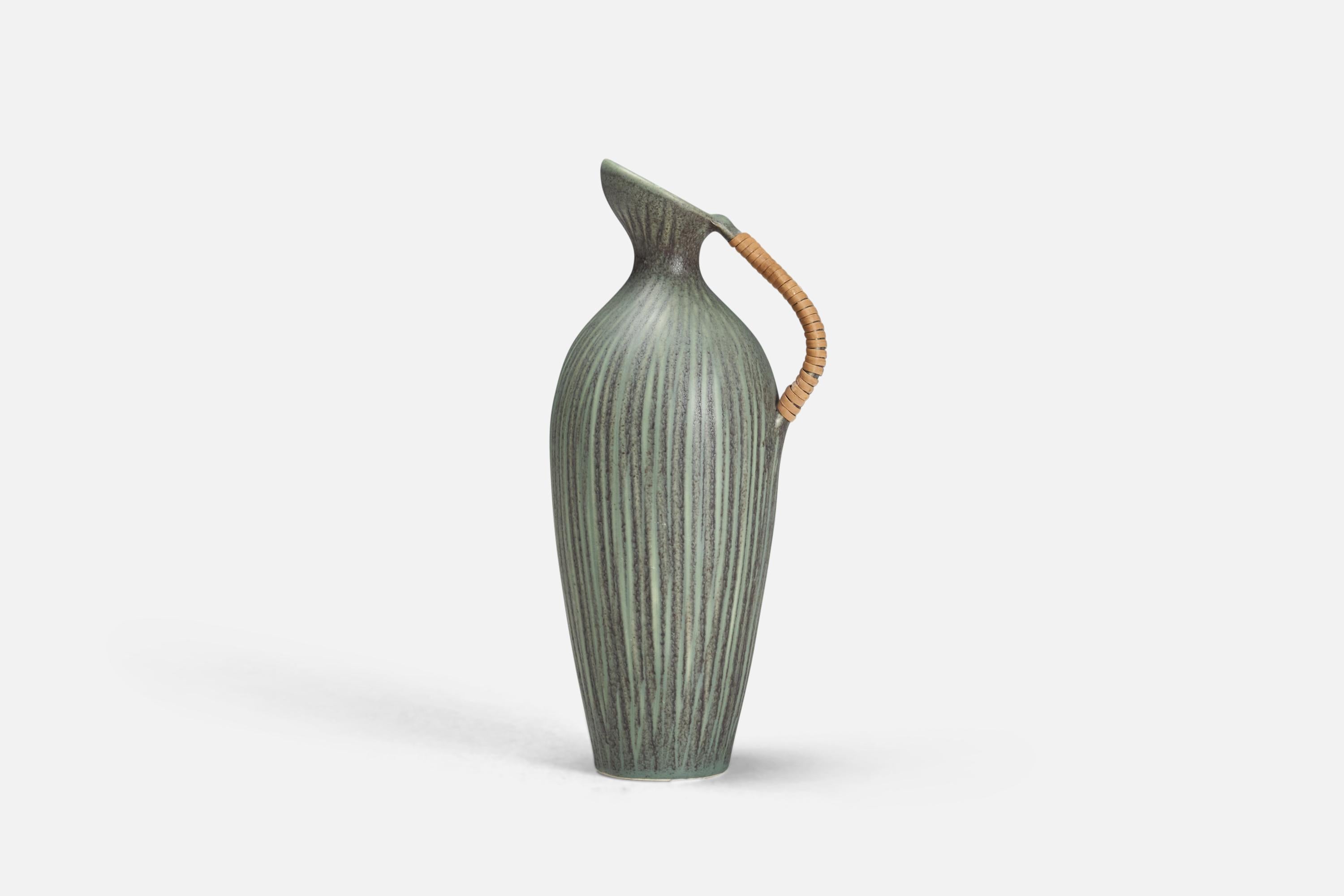 A modernist pitcher. Designed c. 1960s.

Features green glaze and beige / brown stoneware. Handle wrapped in rattan. Stamped and labeled.