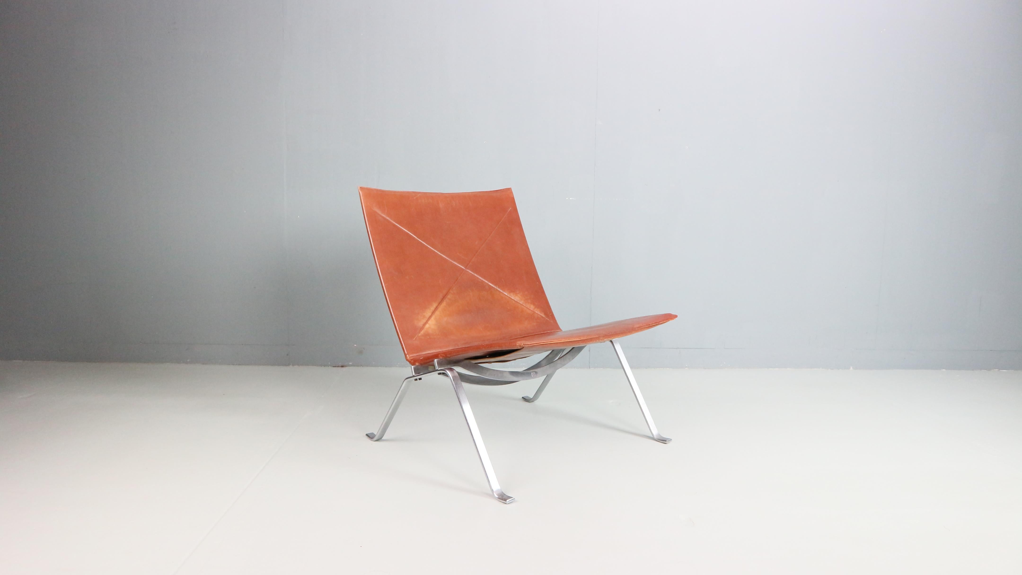 This exquisite PK22 easy chair, designed by Poul Kjaerholm in 1956 for E. Kold Christensen, is a true icon of Danish modern design. A first-edition piece, it features a matte chromed flat steel base and cognac-colored leather seating with a