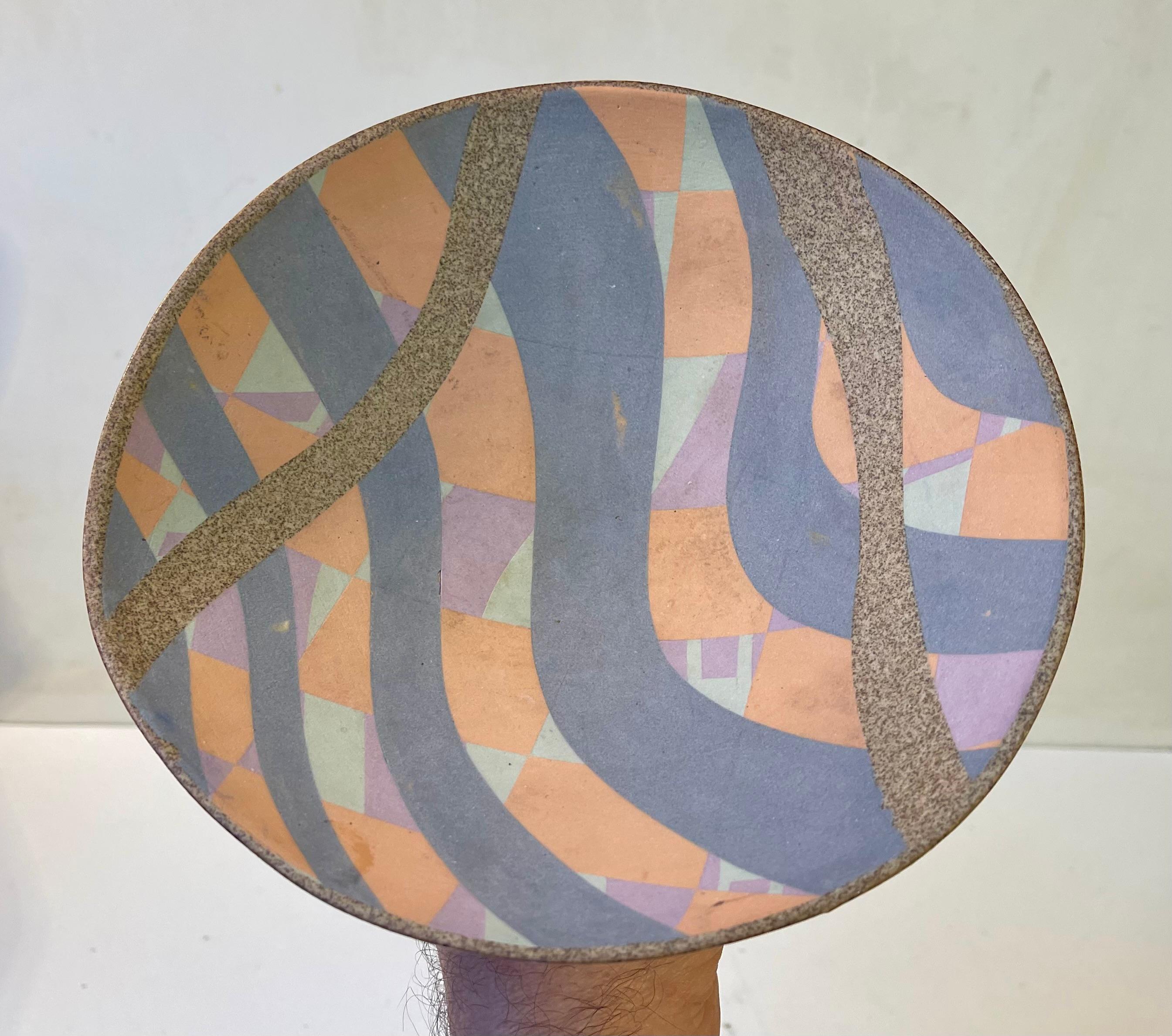 Piatto in gres con piede e bordo asimmetrico. Decorato con colori pastello rosa polveroso, viola prugna, salmone e verde chiaro. Ceramista non identificato in stile postmoderno per B&G in Danimarca, circa 1970-80. Completamente firmata/marcata ecc.