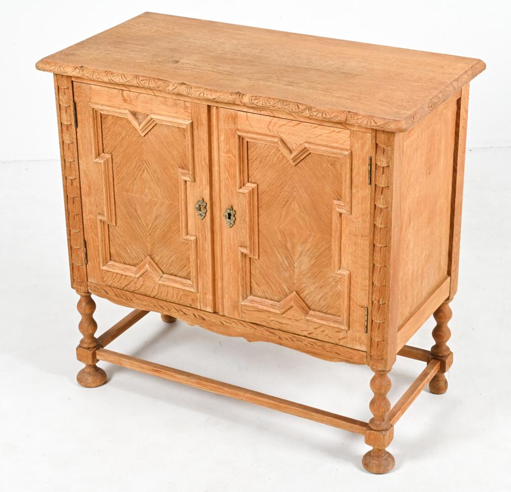 Beautiful storage cabinet in quarter-sawn white oak, featuring Gothic-inspired recessed panel doors, sculpted legs and incised carving at the top trim. Designed by the enigmatic Danish architect Henning Kjærnulf. 

Key included. 

Henning Kjærnulf
