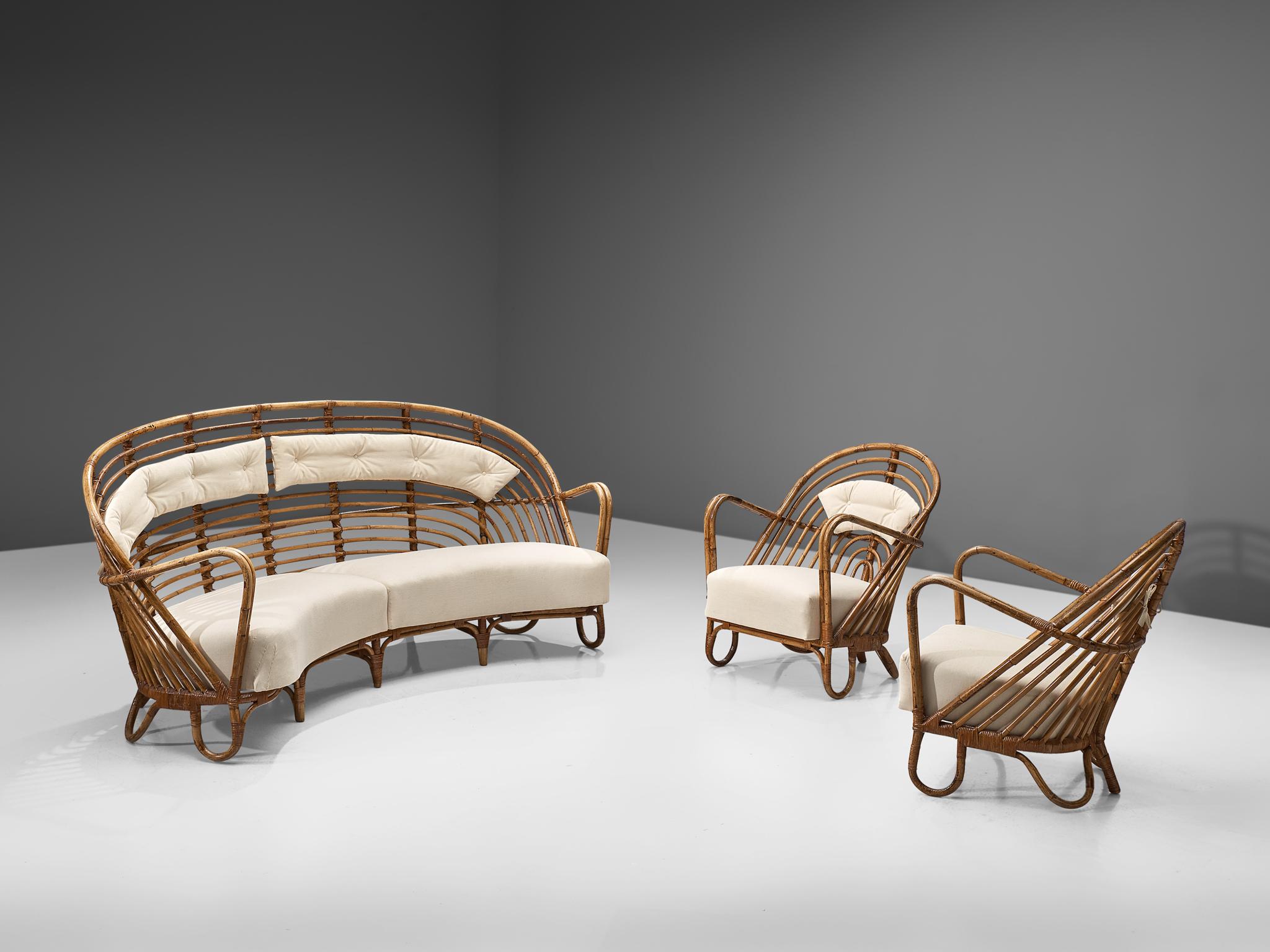 Living room set, rattan and fabric, Denmark, 1936.

Stunning wicker lounge set, consisting of a curved sofa and two lounge chairs. The set features a rounded and airy structure executed in rattan. The seats are slightly curved and feature thick