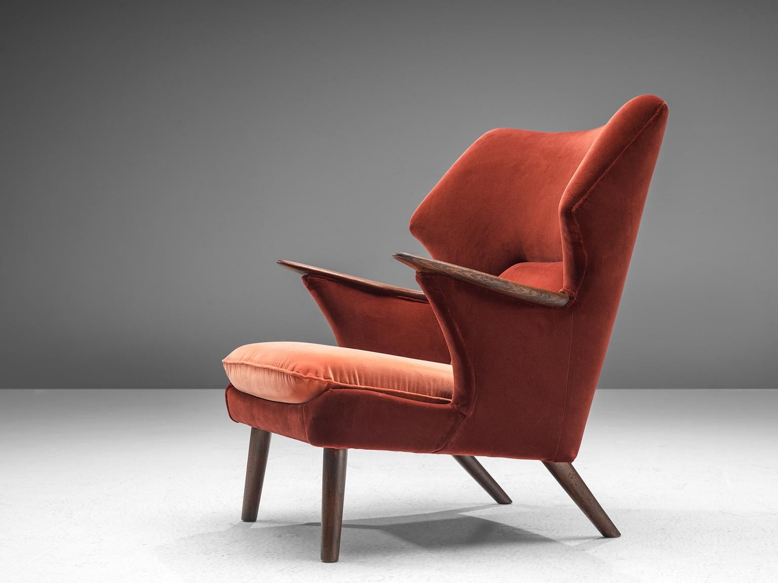 Wing Back chair, red velvet and darkened oak, Denmark, 1950s.

Beautiful Danish wingback chair with a notable design. The back with wide ears create an intimate feeling for the sitter. The long armrests are finished with a wooden top, that