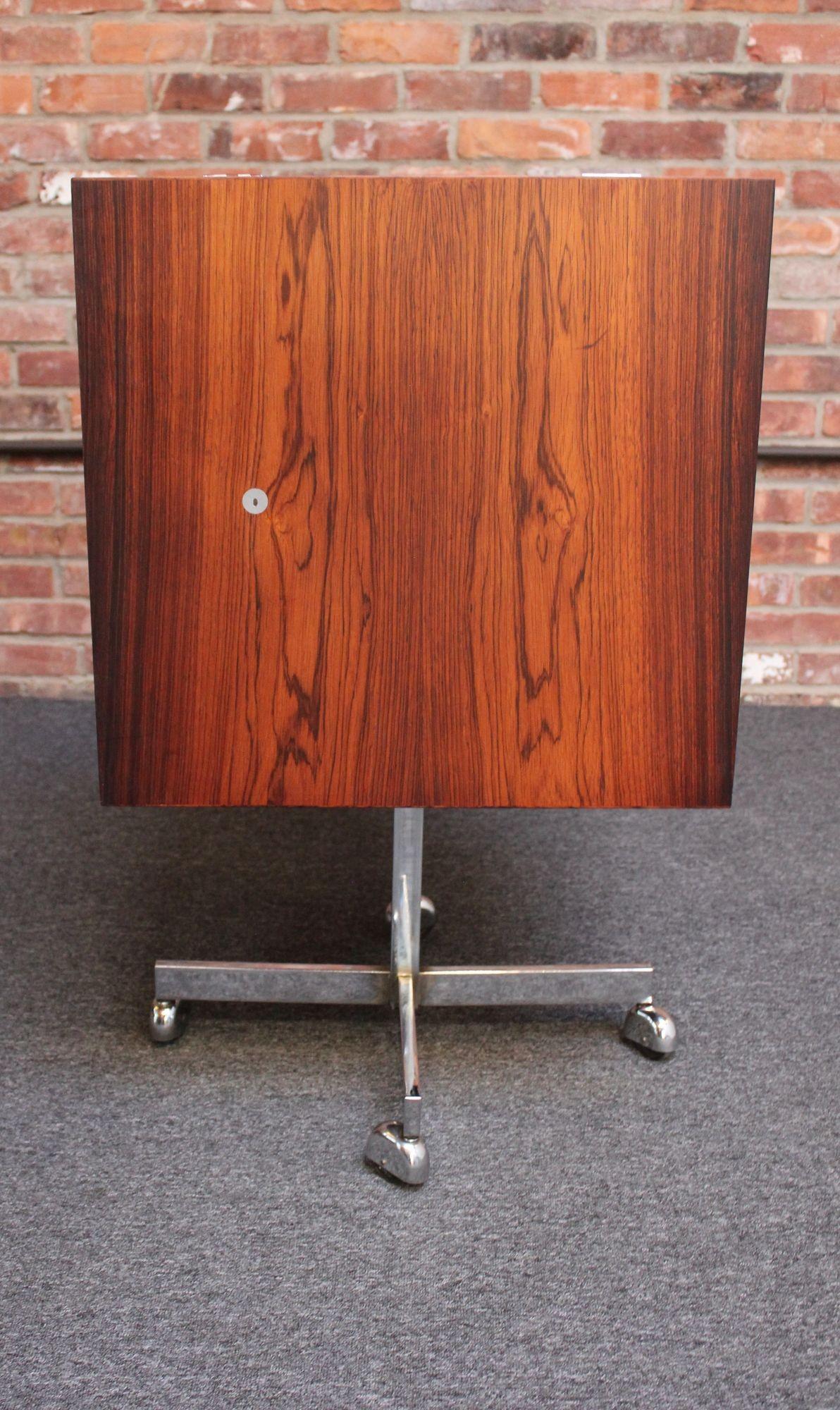 Rosewood dry bar supported by chrome base with caster wheels designed by Poul Nørreklit for Georg Petersens Møbelfabrik (ca. 1960s, Denmark).
Ingenious design featuring a spring-loaded mechanism which raises the cube roughly 10