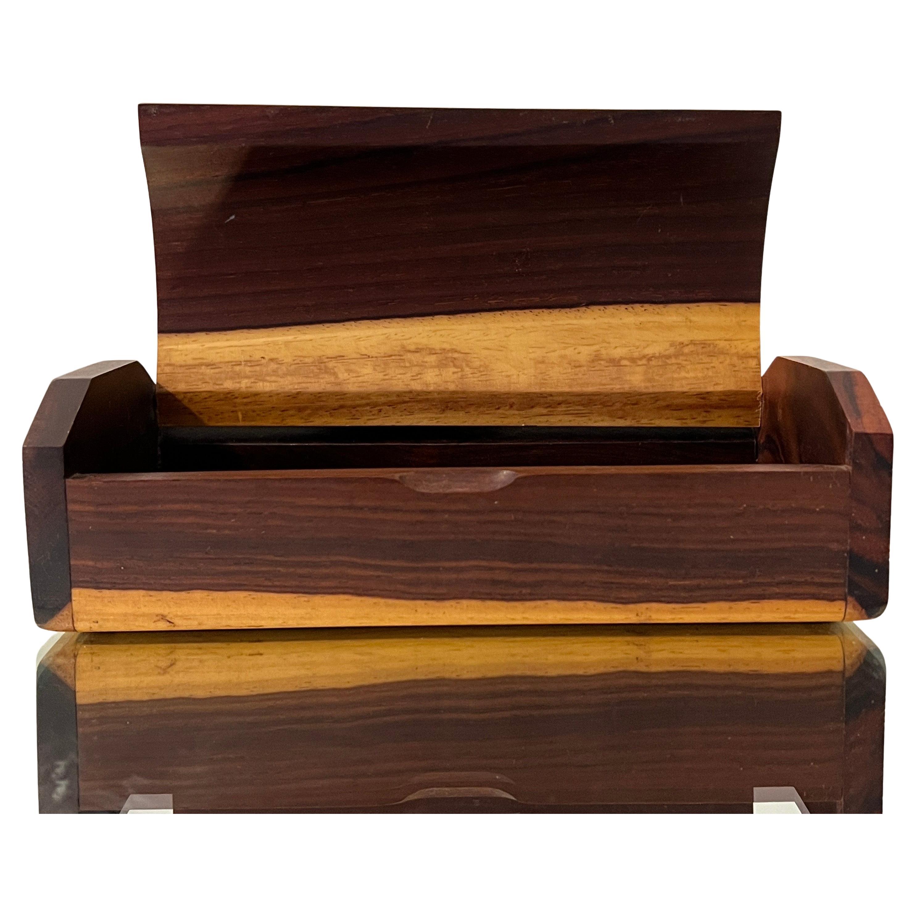 Esta bonita caja decorativa de la Modernidad de Mediados de Siglo está hecha a mano con maderas duras y presenta principalmente palisandro con elementos de madera de arce. La parte superior de tres lados tiene una tapa abatible que se abre a un
