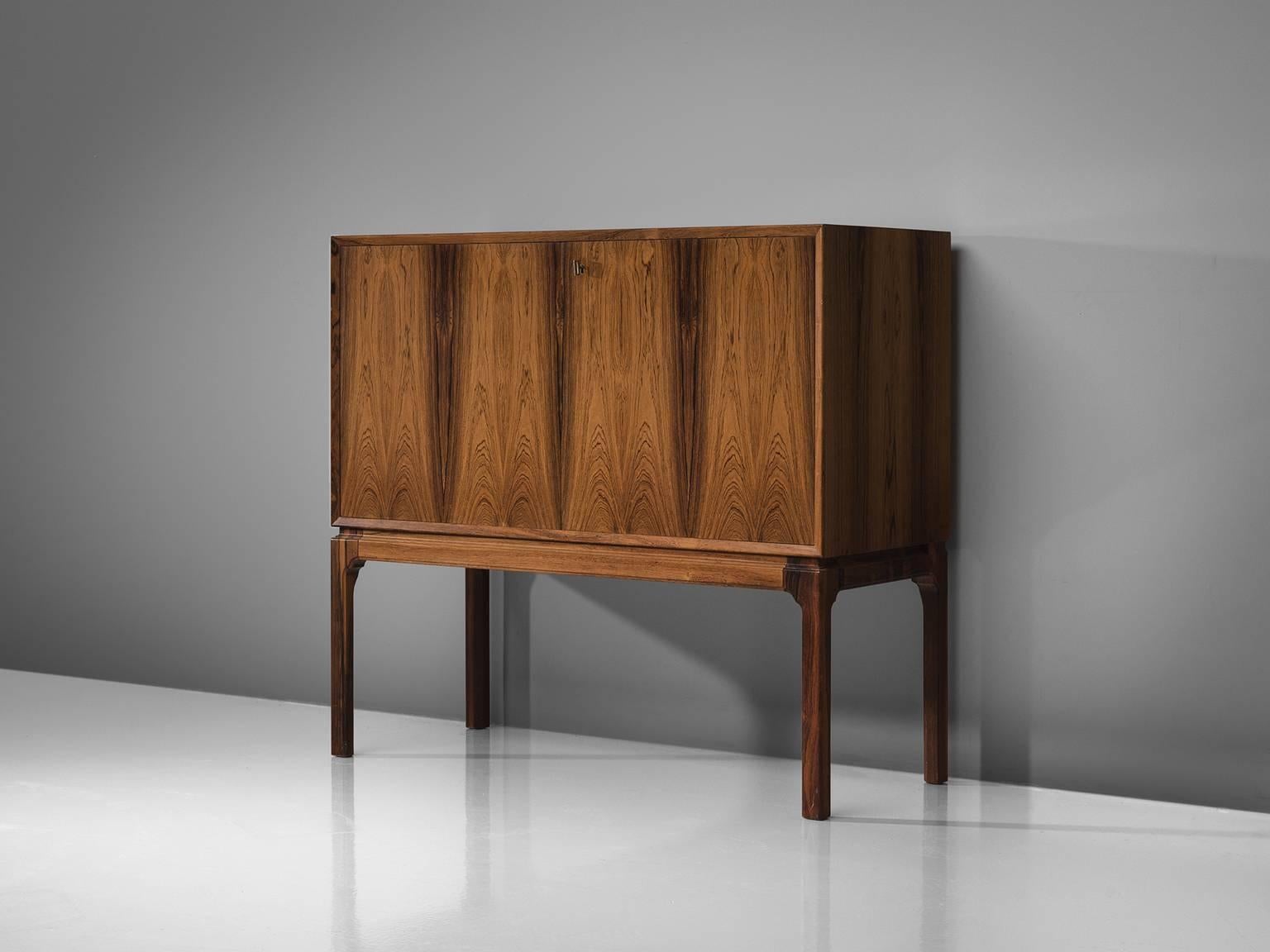 Dry bar, rosewood, glass, Denmark, 1950s. 

This playful, delicate bar cabinet is made out of rosewood. The exterior of this piece is grained and warm. The front holds a bookmatched rosewood front, giving the piece a luxurious appearance. The