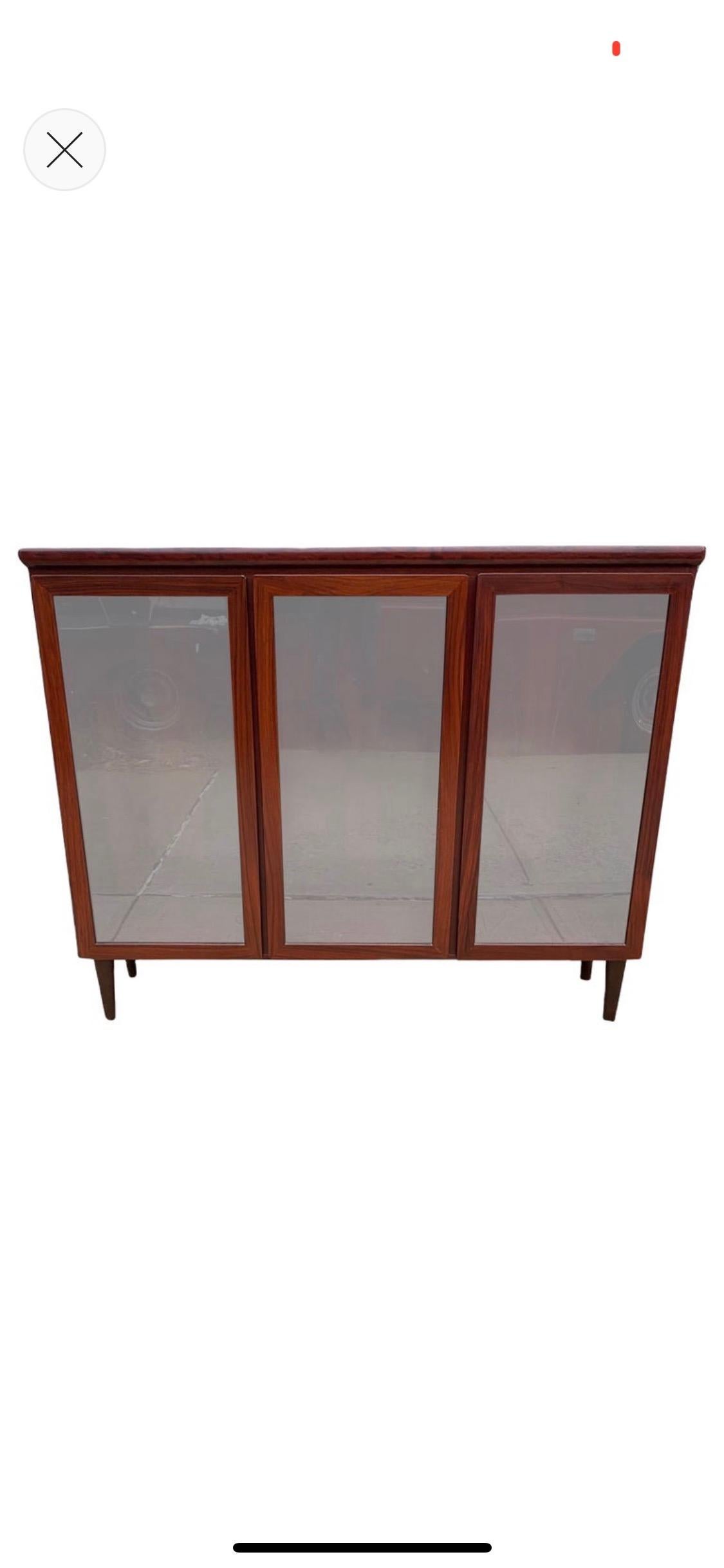 Executed in Brazilian rosewood, this cabinet bookshelf has three glass door cabinets with adjustable glass shelving to provide ample storage. Stunning rosewood grain and color. The cabinet is wired and features a light inside. Signed with original