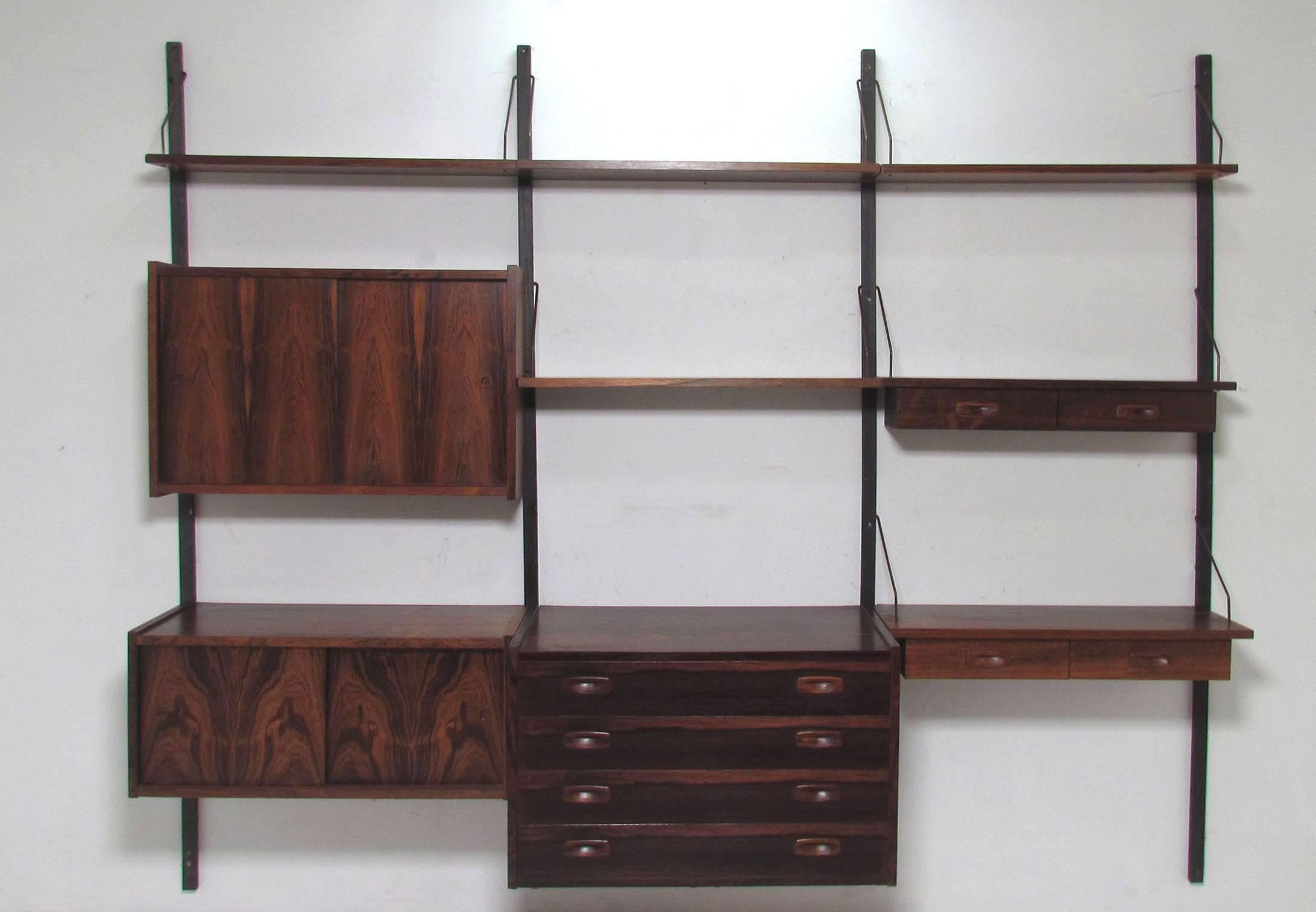 Danish rosewood wall-mounted shelving unit designed by Preben Sorensen, PS System for Randers, circa 1960s. Three bay unit consists of cabinets, drawer space and shelving. 

All components are 31 3/8