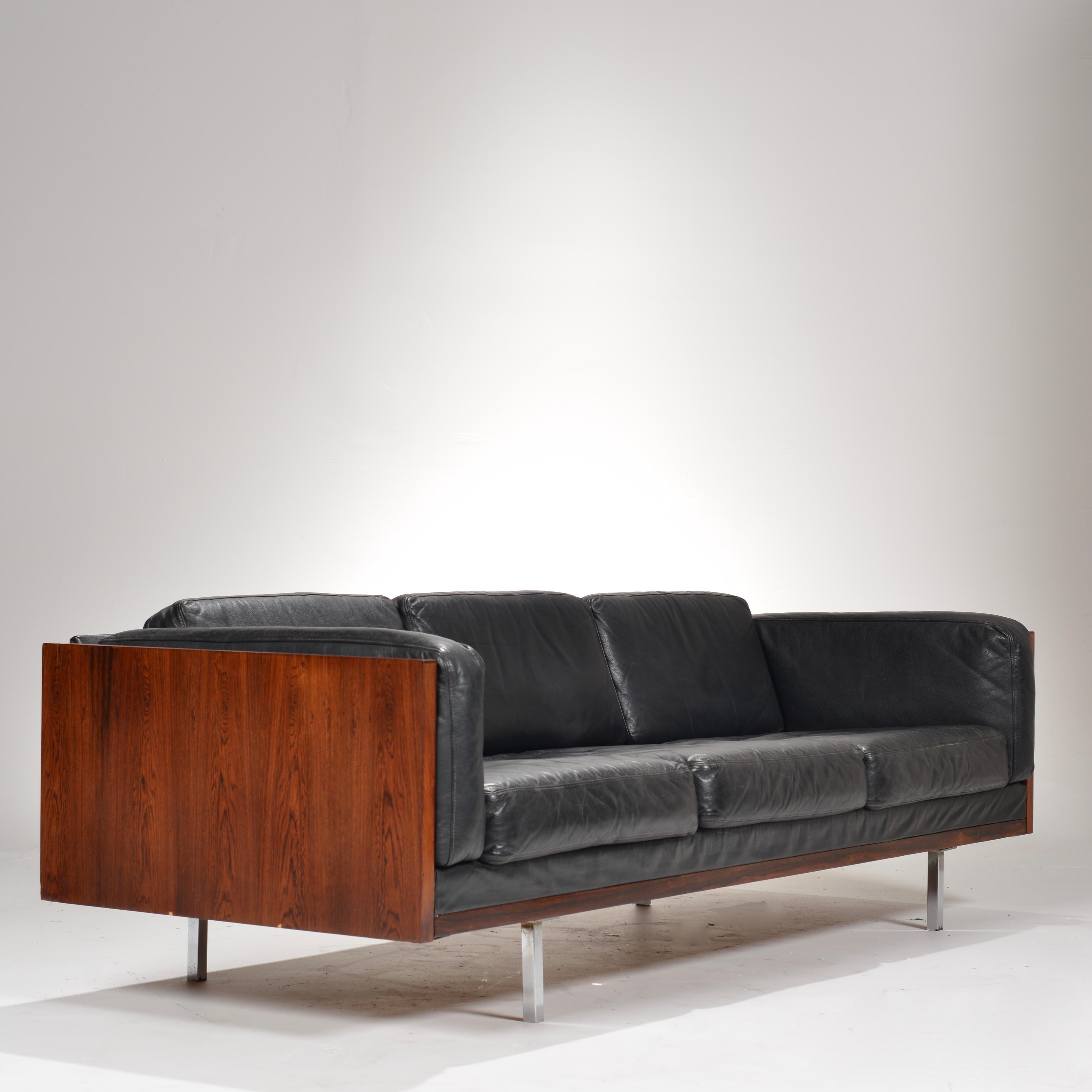 Amazing rosewood case sofa by Comfort of Denmark. The sofa has a three-sided case in boldly figured Brazilian rosewood, and the long, horizontal design appears to float above the ground on four chrome-plated square legs.