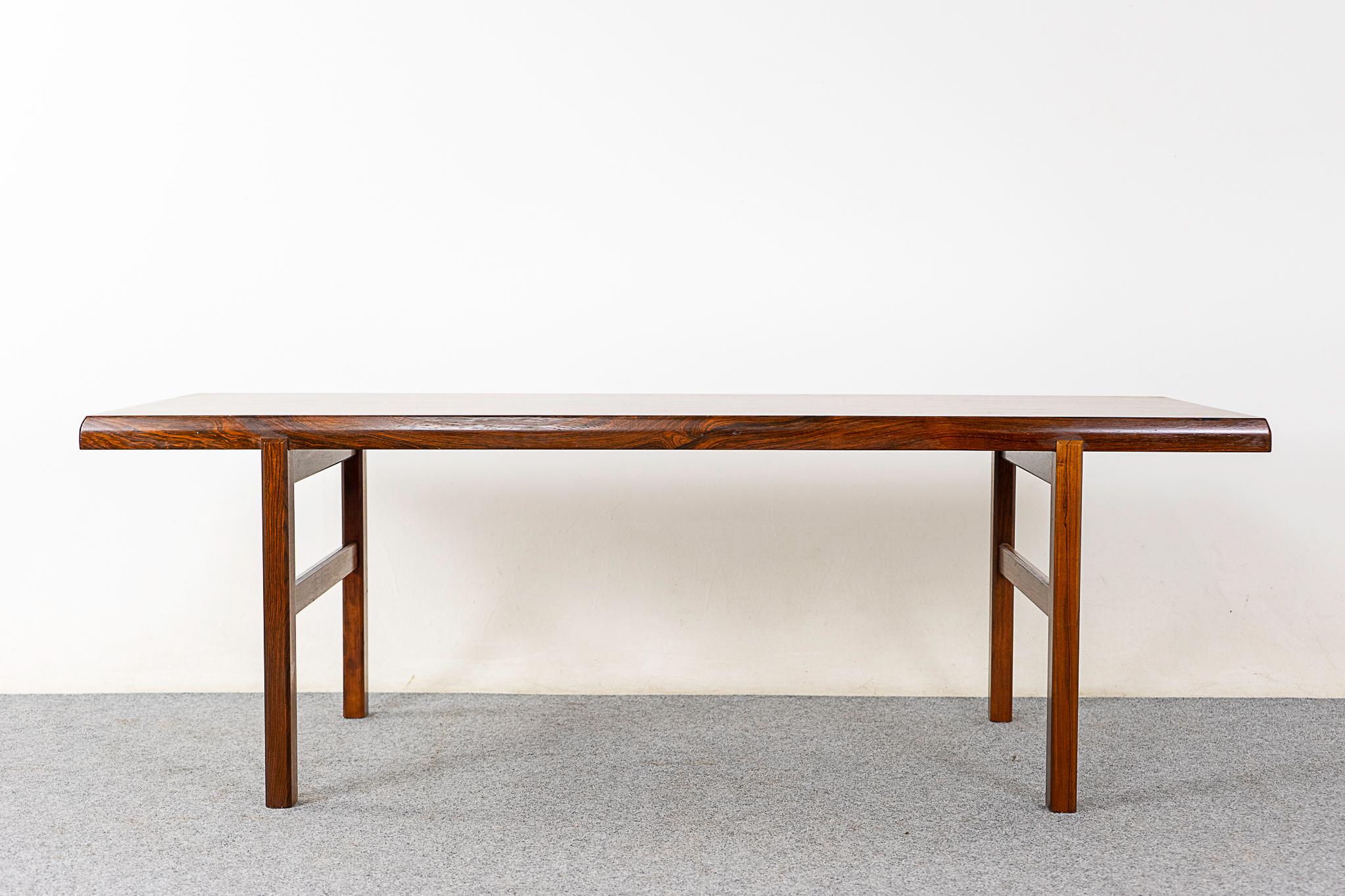 Rosewood mid-century coffee table, circa 1960's. Beautiful book matched veneer on the top surface with a solid wood curved edge along its length. Cross bars for additional stability and longevity. 