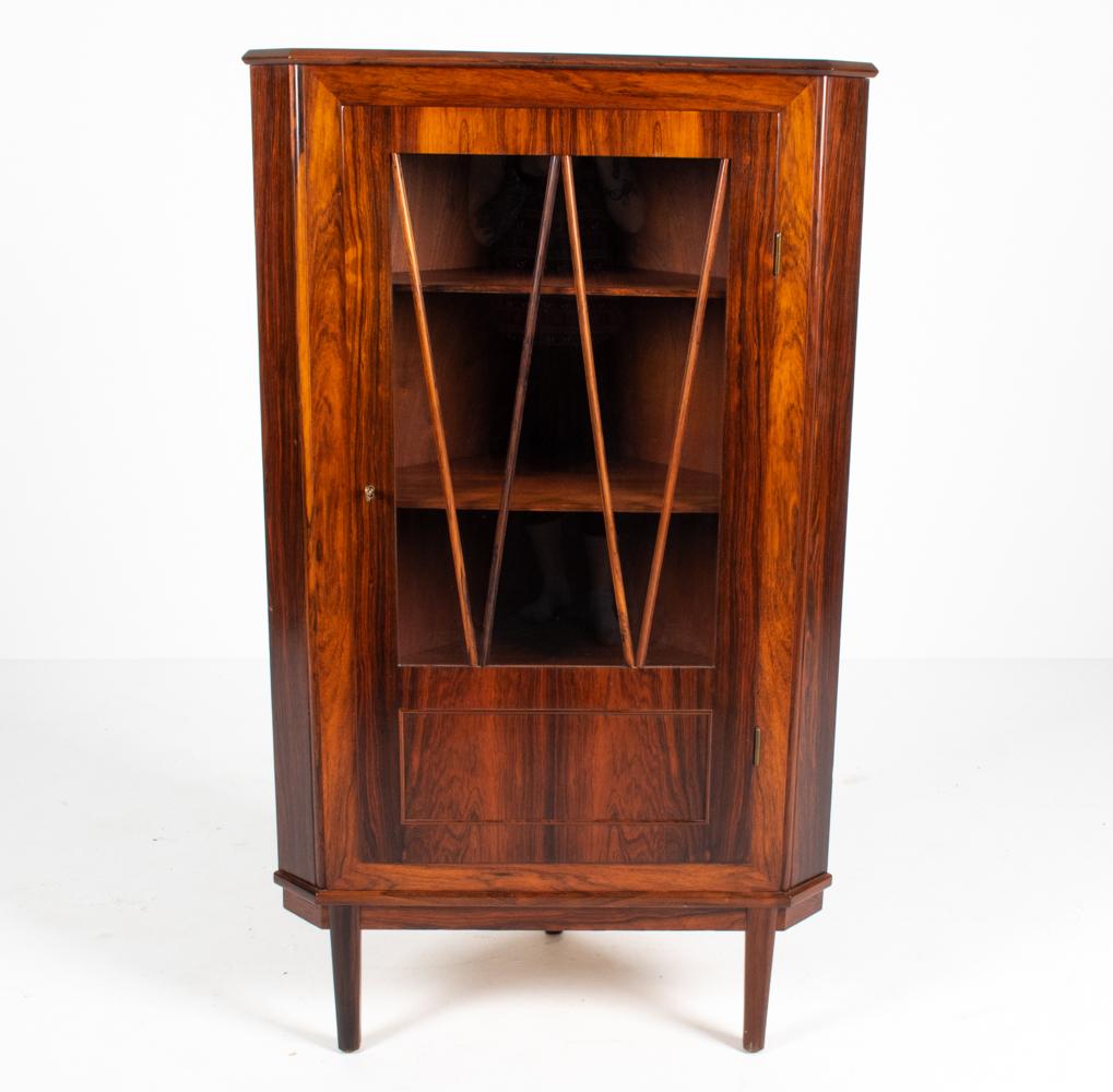 This Danish 20th century corner cabinet is sure to impress with its stunningly figured rosewood veneer. With a glass front and shelved interior, this cabinet would make a handsome vitrine to display your collectibles or a fabulous bar. c.