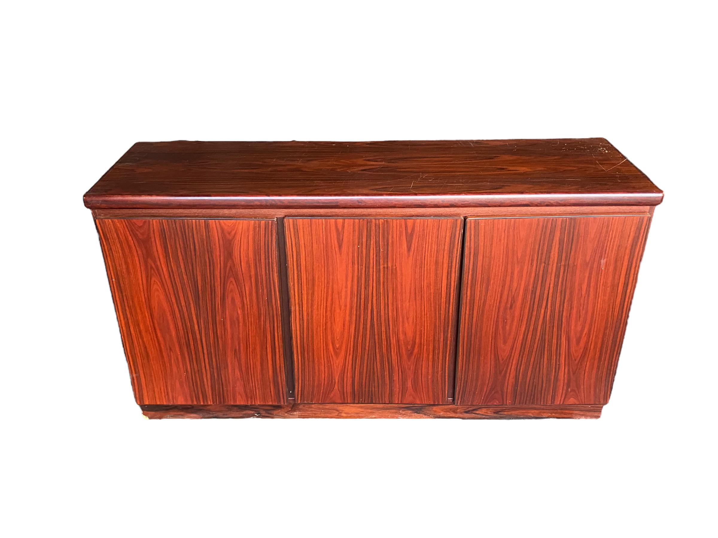 Danish modern credenza sideboard in rosewood. Manufactured by Rasmus Furniture, this piece has three storage compartments, two connecting with shelves and one separate door with drawers. Elegant, simple design with stunning rosewood grain. 