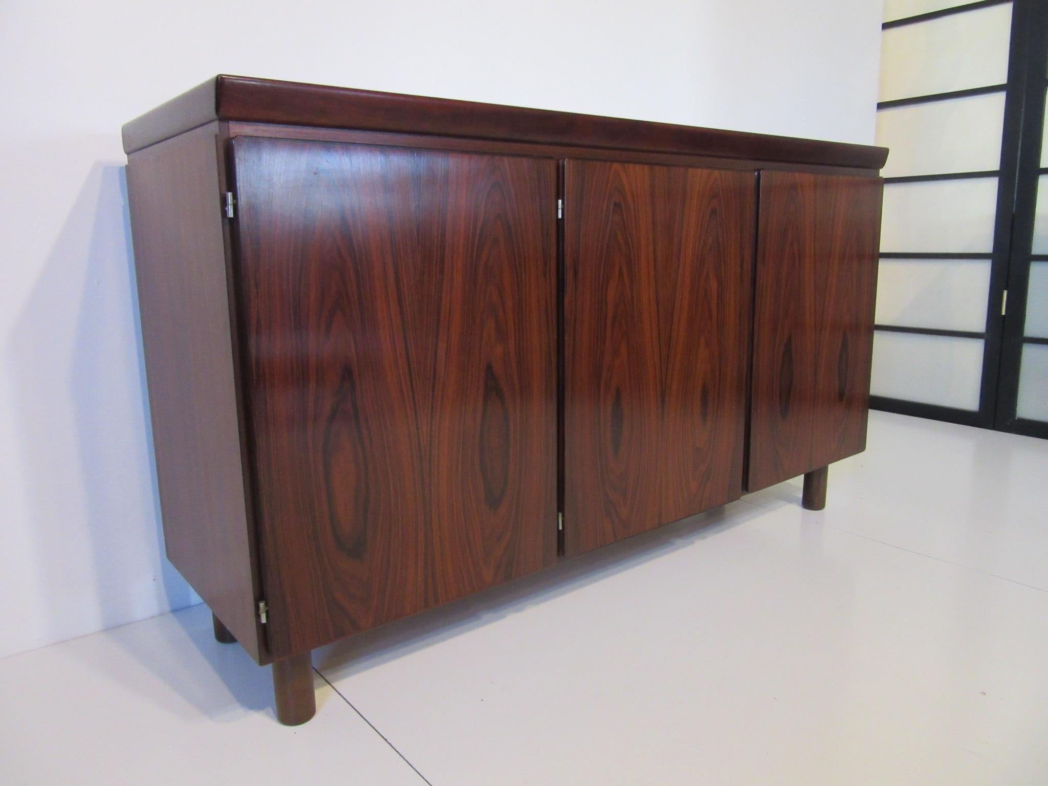 A dark and richly toned Brazilian rosewood credenza or server with five smaller drawers behind the first door and one adjustable shelve behind the other two doors. Well crafted and retaining the makers tag to the back Skovby Mobelfabrik A/S Denmark