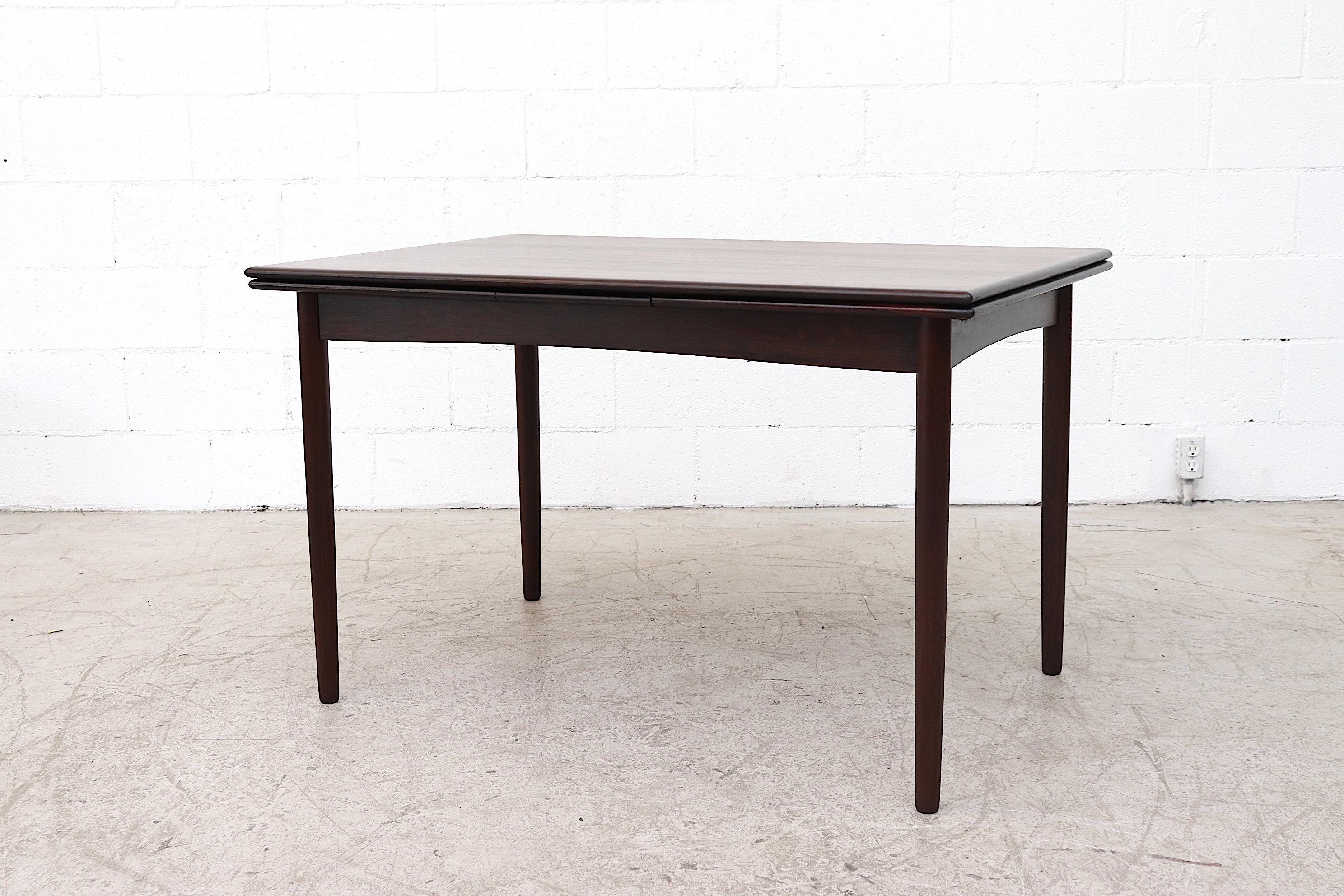 Beautiful rosewood dining table with round tapered legs and slide-out leaf extension. Beautiful grain, lightly refinished and slide to extend leaves. In good original condition with wear consistent with age and use. Two available, tones may vary