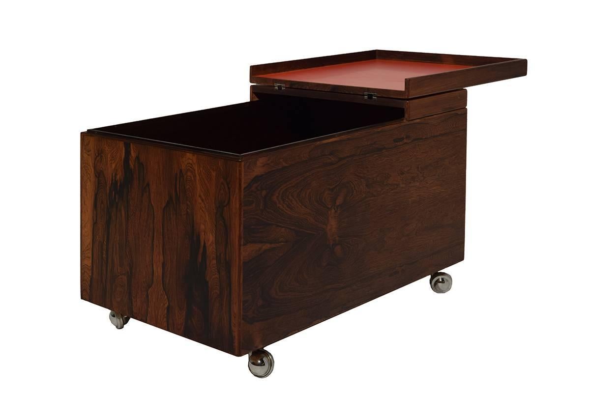 Luxurious and very rare mobile dry bar designed by the Danish Modernist Poul Nørreklit
The top of the bar is easy to fold open. The partly red laminated covered top serves perfectly as a tray.
Complete with Rosewood tray and plenty of space to