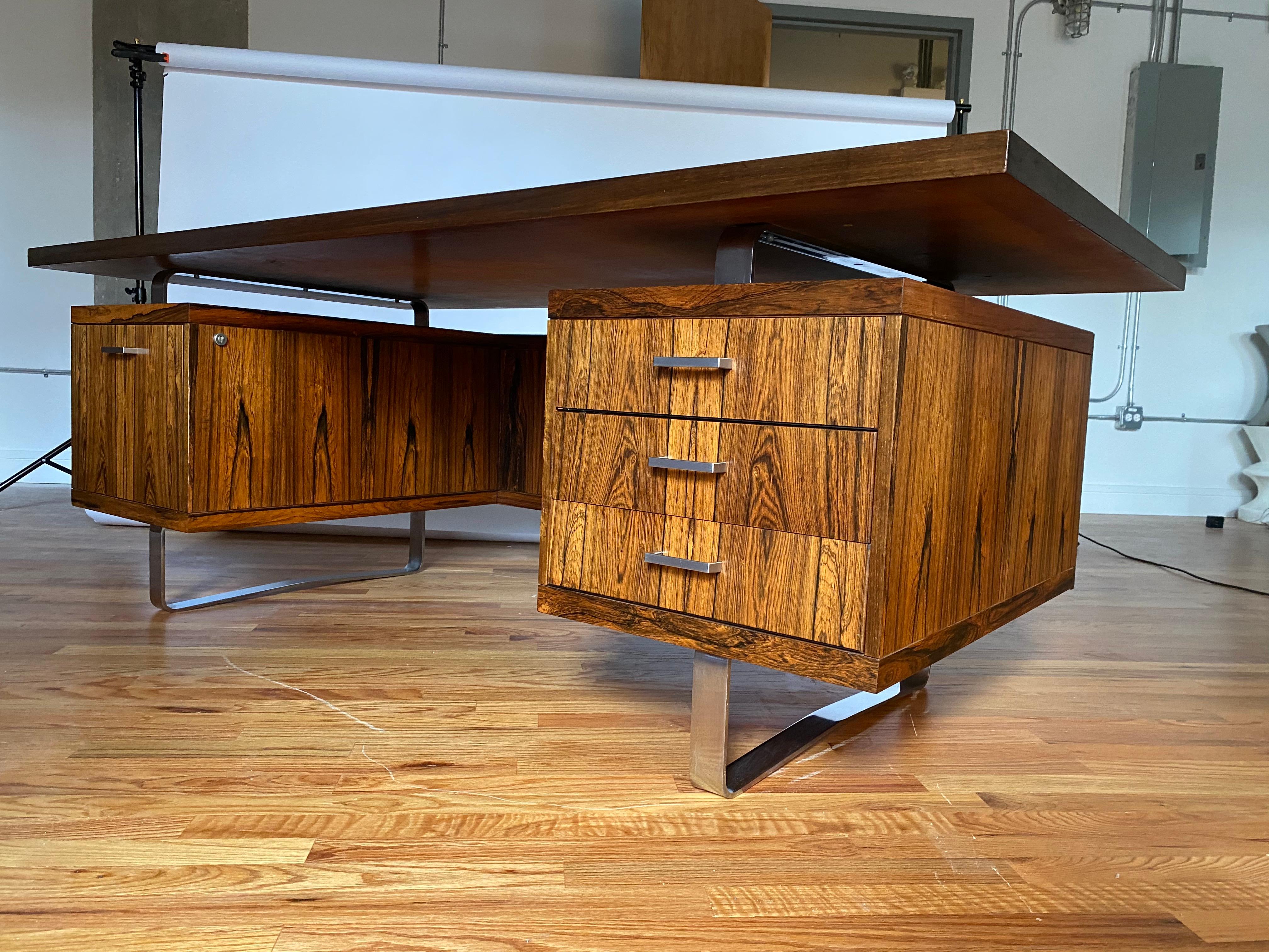 1960s Danish modern rosewood executive desk by Jorgen Pedersen, Denmark. Gorgeous exotic wood grain in magnificent condition for its age with a floating desk top connected by brushed stainless metal hardware and sled legs. Ample storage includes