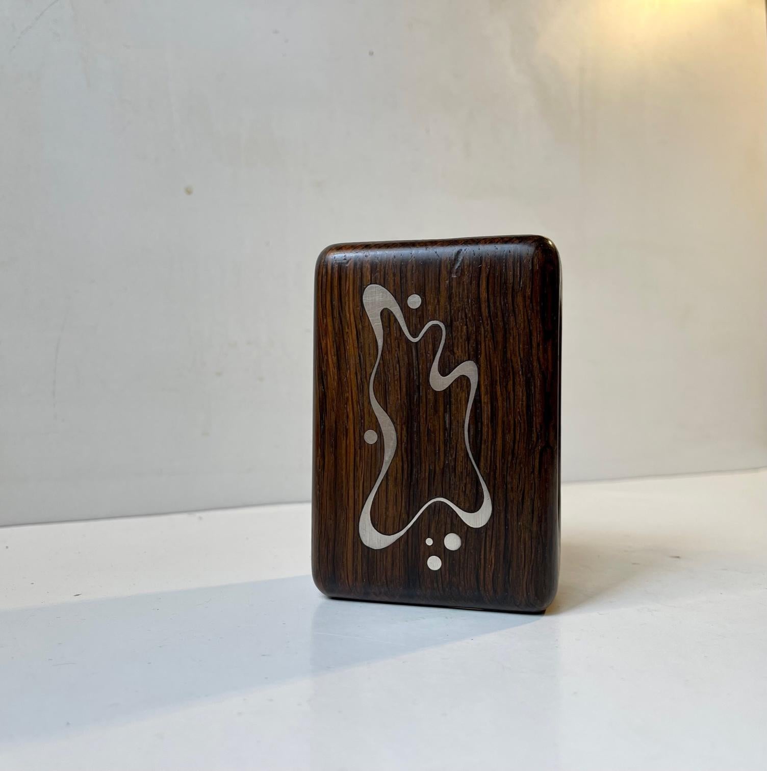 Copenhagen silversmith Axel Salomonsen made a variety of rosewood accessories with sterling silver (925s) intarsia during the late 1950s and 60s. This matchbox holder in solid rosewood features an abstract modernist impression that has been inlaid