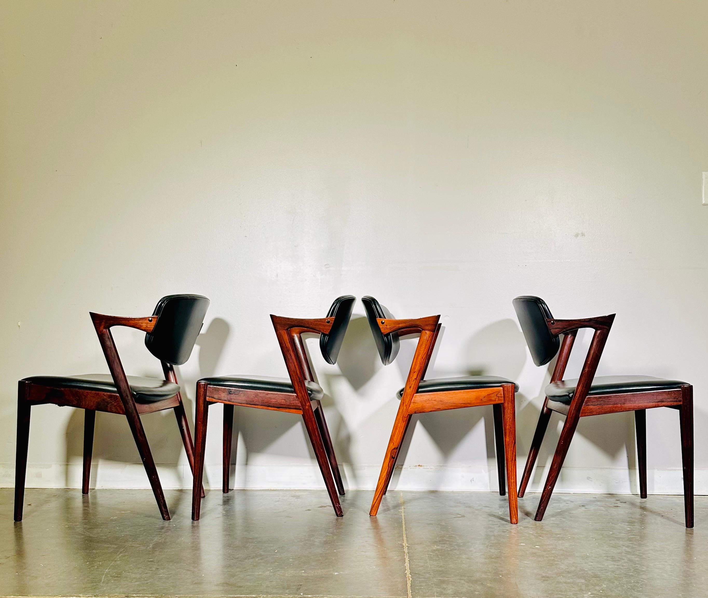 Sillas de comedor vintage Kai Kristiansen modelo 42 de palisandro con tapicería de vinilo negro.

Las sillas son muy cómodas y ofrecen mucho apoyo, con el respaldo curvado que pivota y te permite sentarte formal o reclinado.

Este conjunto de 4