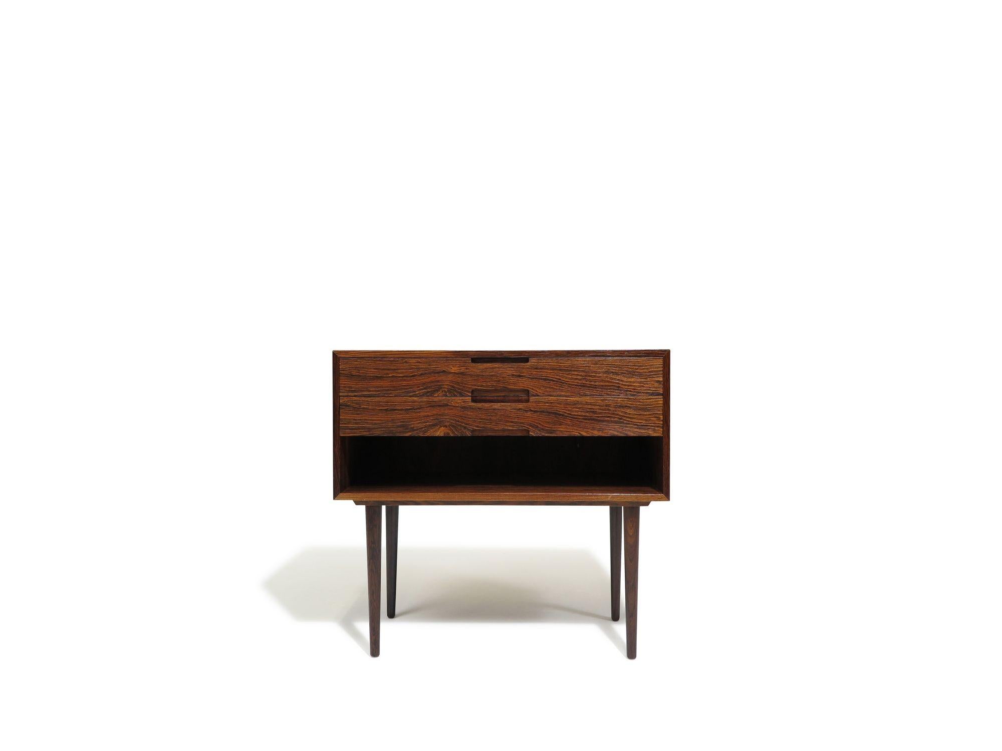 Pair of mid-century Danish nightstands handcrafted from exotic Brazilian rosewood with dynamic, pattern-matched grain and mitered edges. Each unit includes two drawers with recessed pulls above an open lower compartment, and is raised on elegant