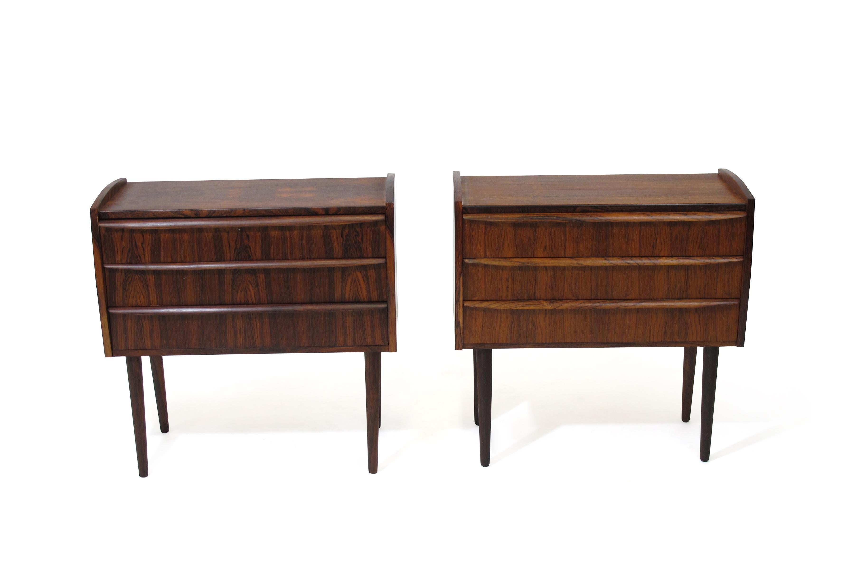 Danish Brazilian rosewood cabinets each with three drawers and carved pulls, book-matched grain, and raised on stilted legs. The cabinets have been fully restored in a natural oil finish and in excellent condition with minor sign of age and use.