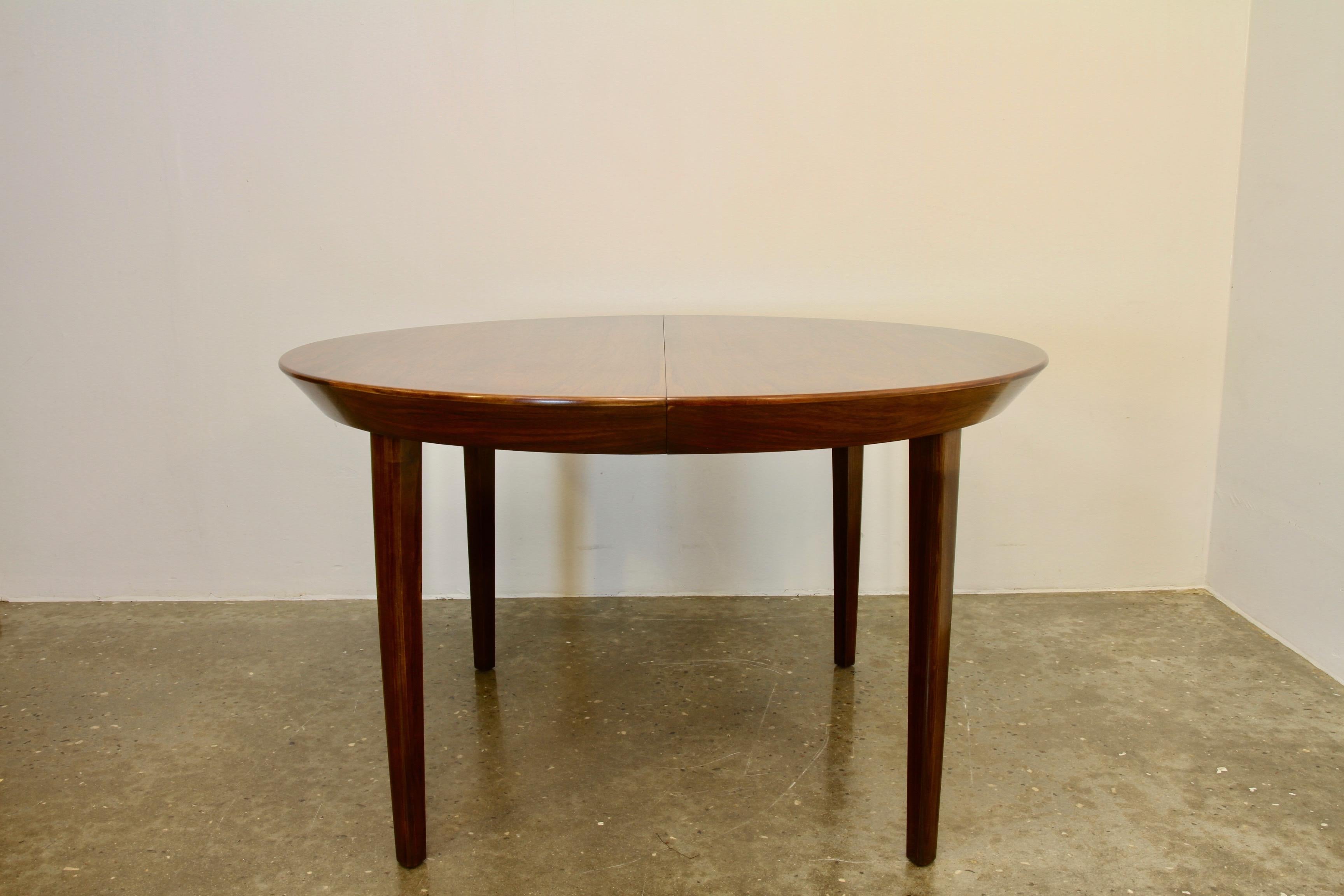 Immensely beautiful and elegant Danish Mid-Century Modern extendable round dining table. Very stylish large slanting edge and tapered legs. Amazing mirrored veneer vintage pattern. Comes with two extension leaves each 49.5 cms, which increases the