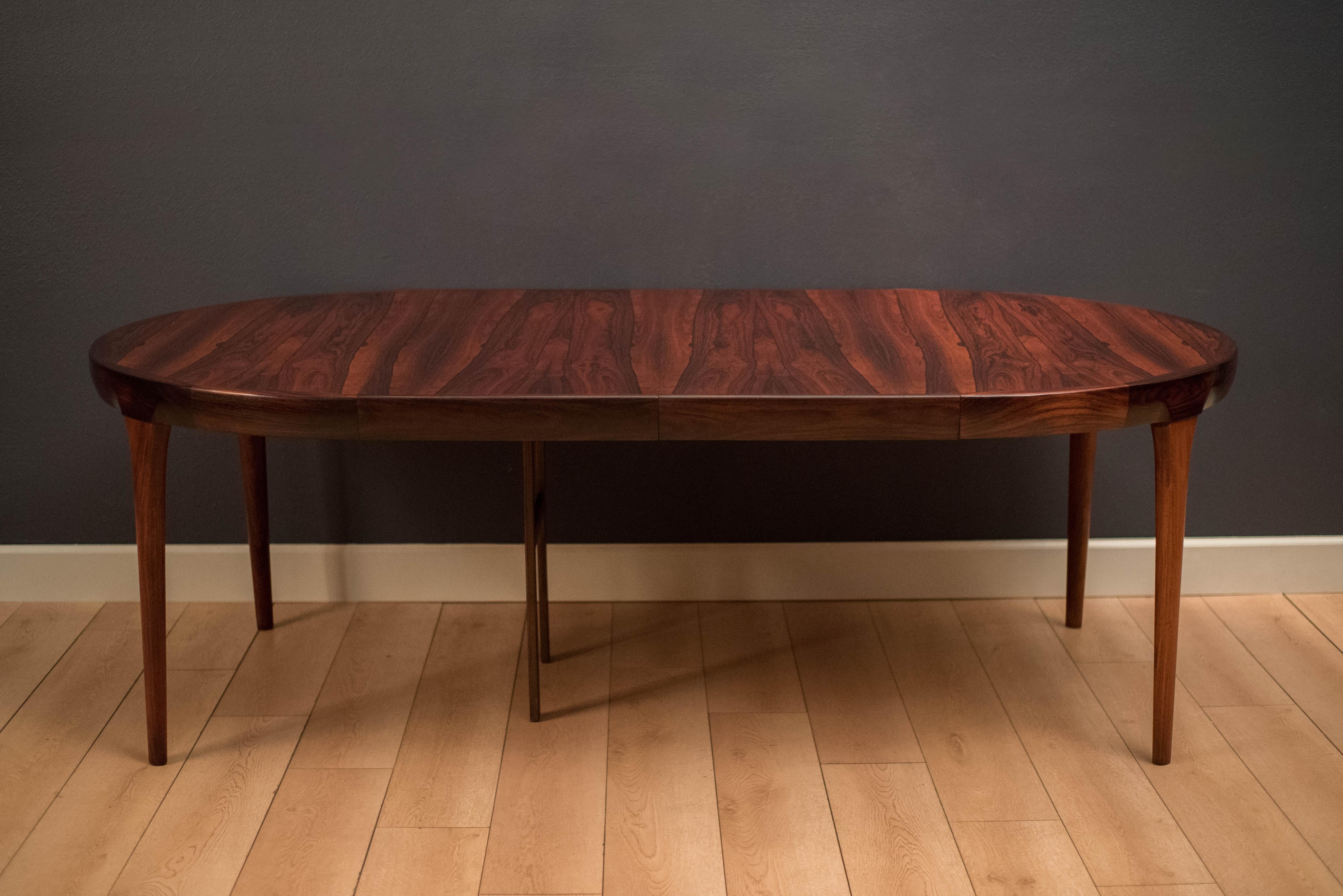 Mid-Century Modern dining table designed by Ib Kofod-Larsen for Faarup Mobelfabrik. This piece displays continuous Brazilian rosewood grains and solid edge banding with a seamless sculpted apron. The table extends with two leaves and can fit up to