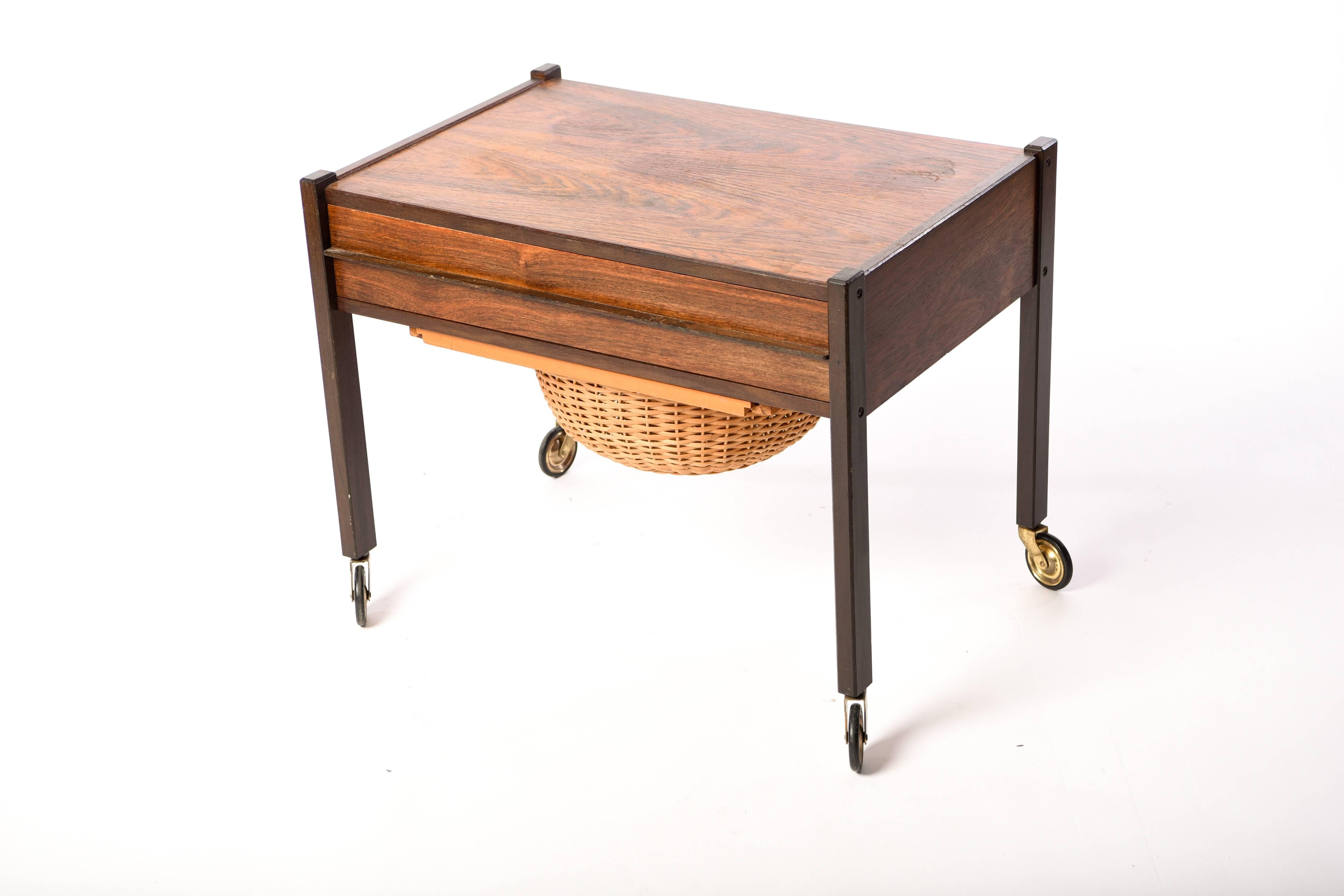 This Danish midcentury rosewood sewing table features wheels for easy mobility and a storage basket underneath.