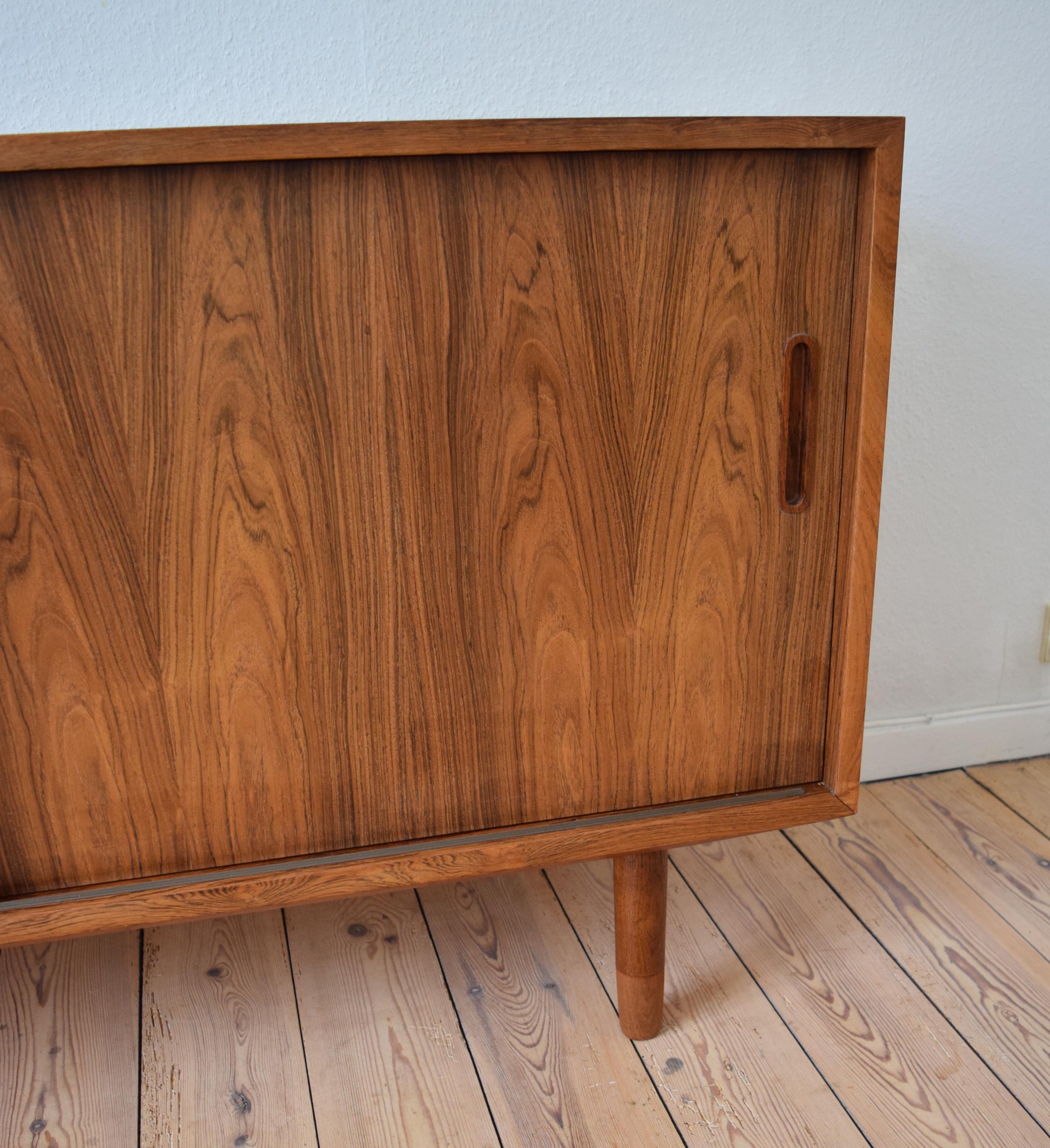 Low rosewood sideboard by Carlo Jensen for Poul Hundevad manufactured in Denmark in the 1960s. This piece features two sliding doors with solid rosewood handles, two felt lined maple drawers and two shelves. Sits on turned and tapered two-tone