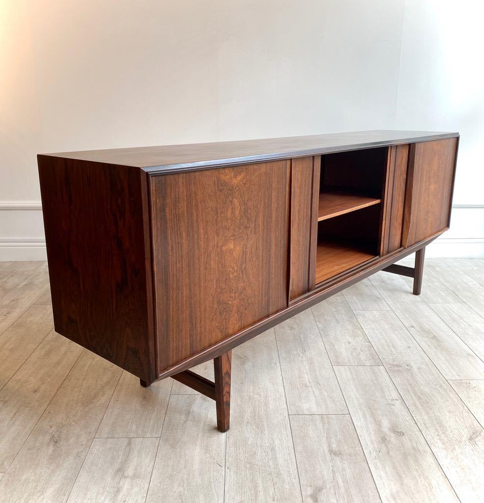 Low Brazilian rosewood sideboard designed by E.W. Bach manufactured by Sejling Skabe in Denmark in the 1960s. 

Four smooth sliding doors on the front with three internal compartments with shelves and drawers. 

Rare example of a much sought