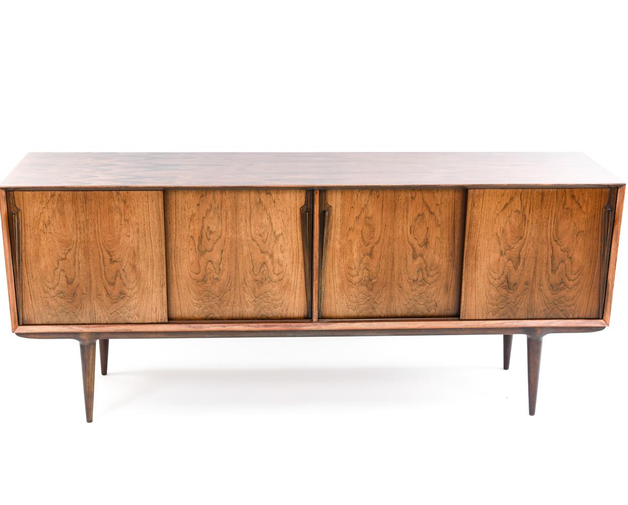 This gorgeous rosewood sideboard was designed by Gunni Omann for Omann Jr. The bevel-edged case sits on tapered legs and features four sliding doors with long organic handles. Inside are two adjustable shelves and, to the left, six felt-lined tray