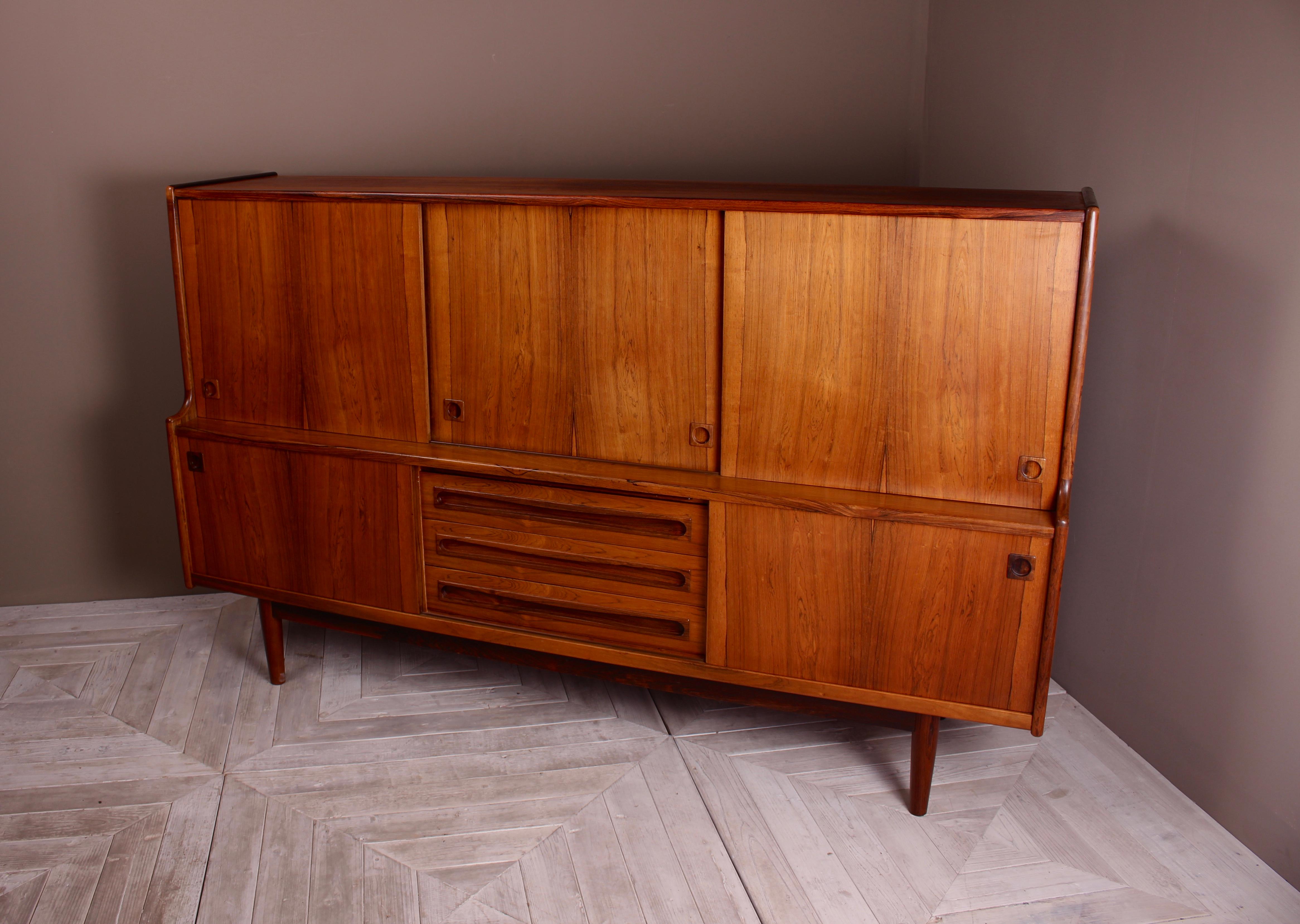 An attractive midcentury rosewood sideboard by Danish cabinet maker and designer Johannes Andersen. The upper section with oak and baize lined slide trays to the left, adjustable shelves to left and center. The lower section holding three central