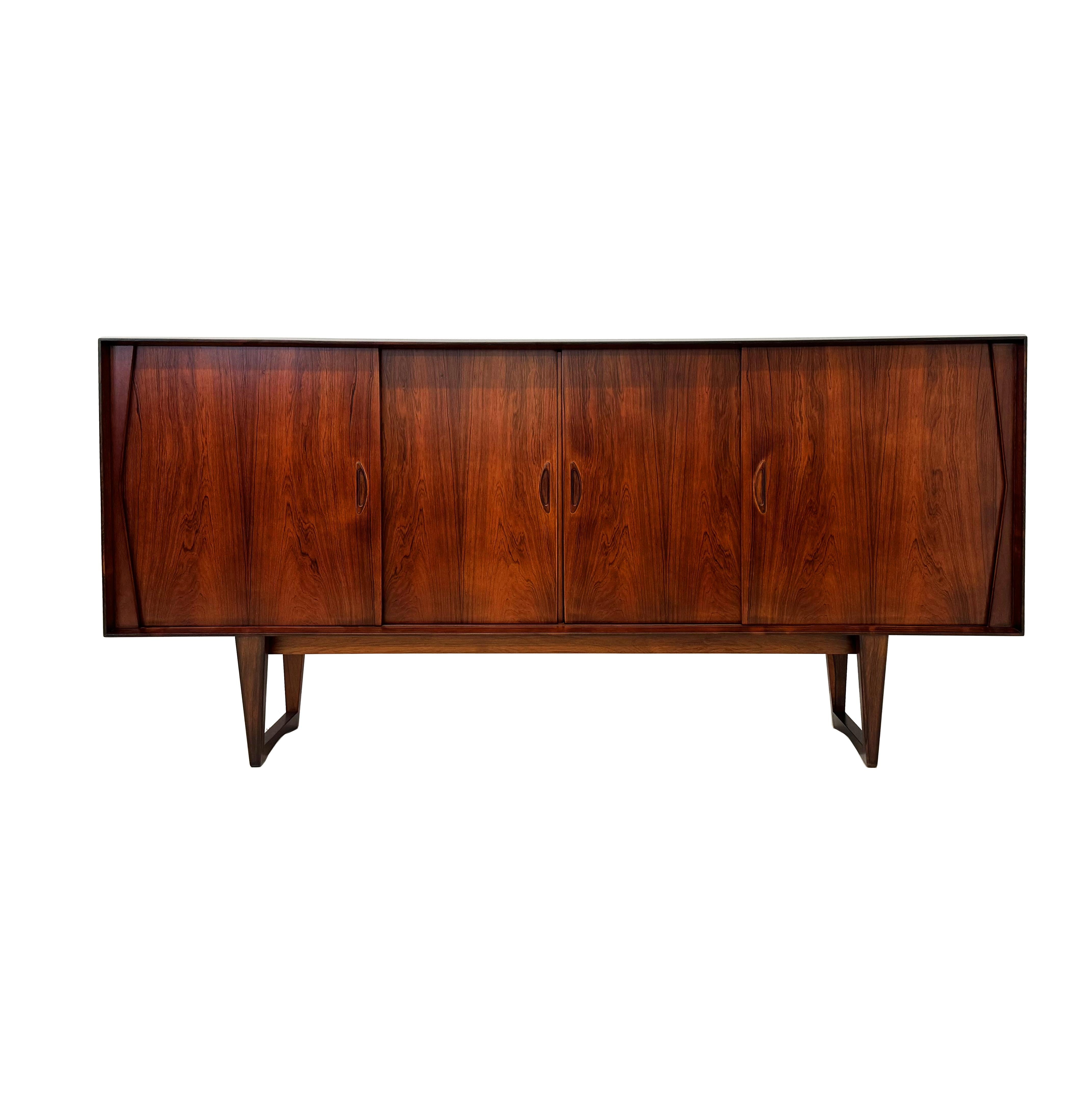 Mid-Century Brazilian Rosewood sideboard with dynamic book-matched grain on four sliding doors. Nice detailed legs. Shelves, three drawers and a bar with mirror inside. Adjustable shelves. Light automatically turns on when center doors open, to
