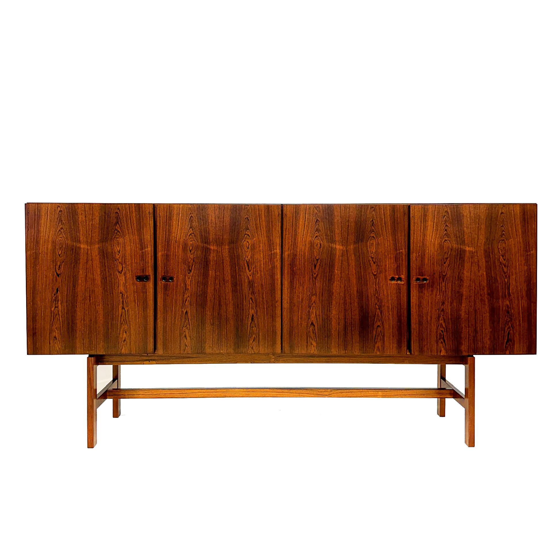 Mid-Century Brazilian Rosewood sideboard with four doors. Nice detailed handles. Adjustable shelves inside.  Three silverware drawers, and a bar with mirror and two drawers.  Light automatically turns on when left door open, to reveal the bar.
Often
