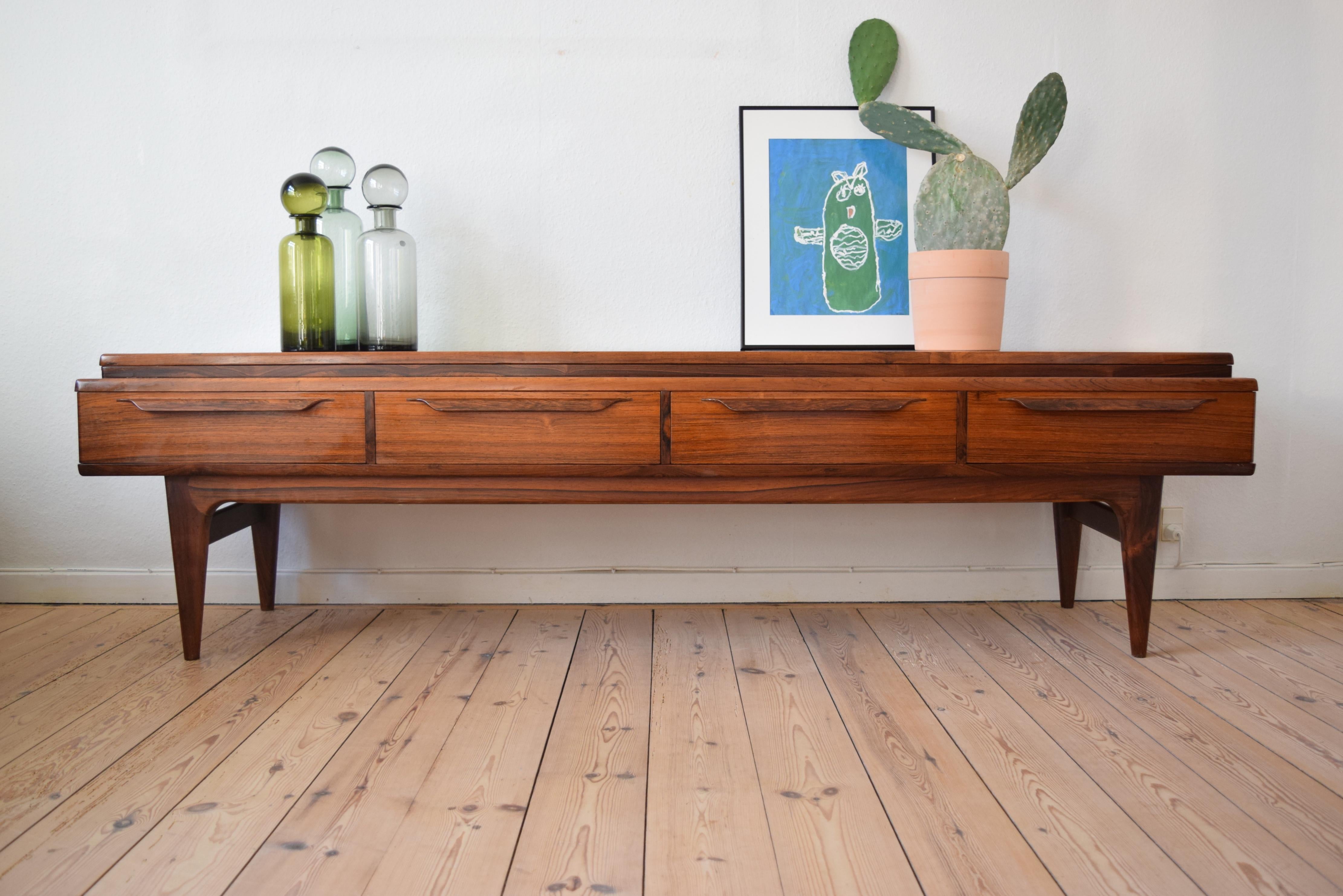 Midcentury rosewood sideboard or media console manufactured in Denmark in the 1960s. Features four drawers on the front with solid rosewood leaf handles. One drawer has an removable insert drawer with felt lining. Sits on rosewood frame base legs.