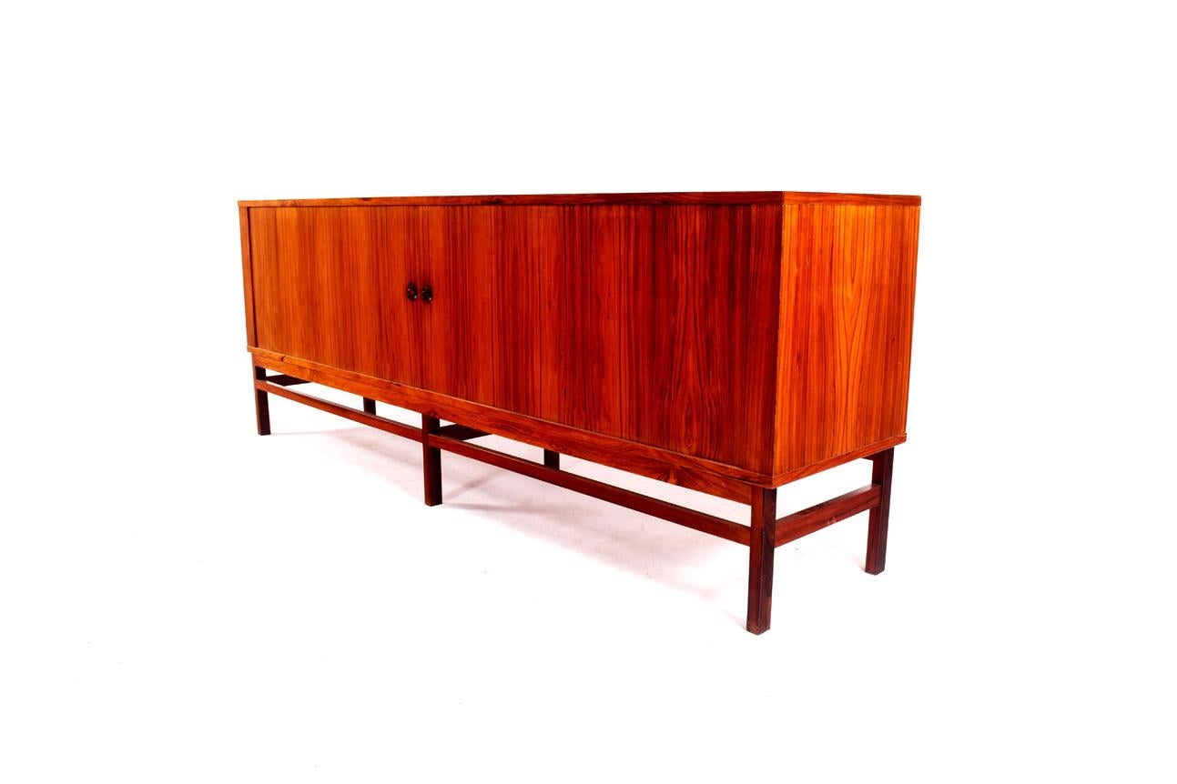 Danish tambour door sideboard in rosewood. Have open cabinets at each end and three shallow drawers at center. This sideboard features a tambour design similar of Hans Wegner's 