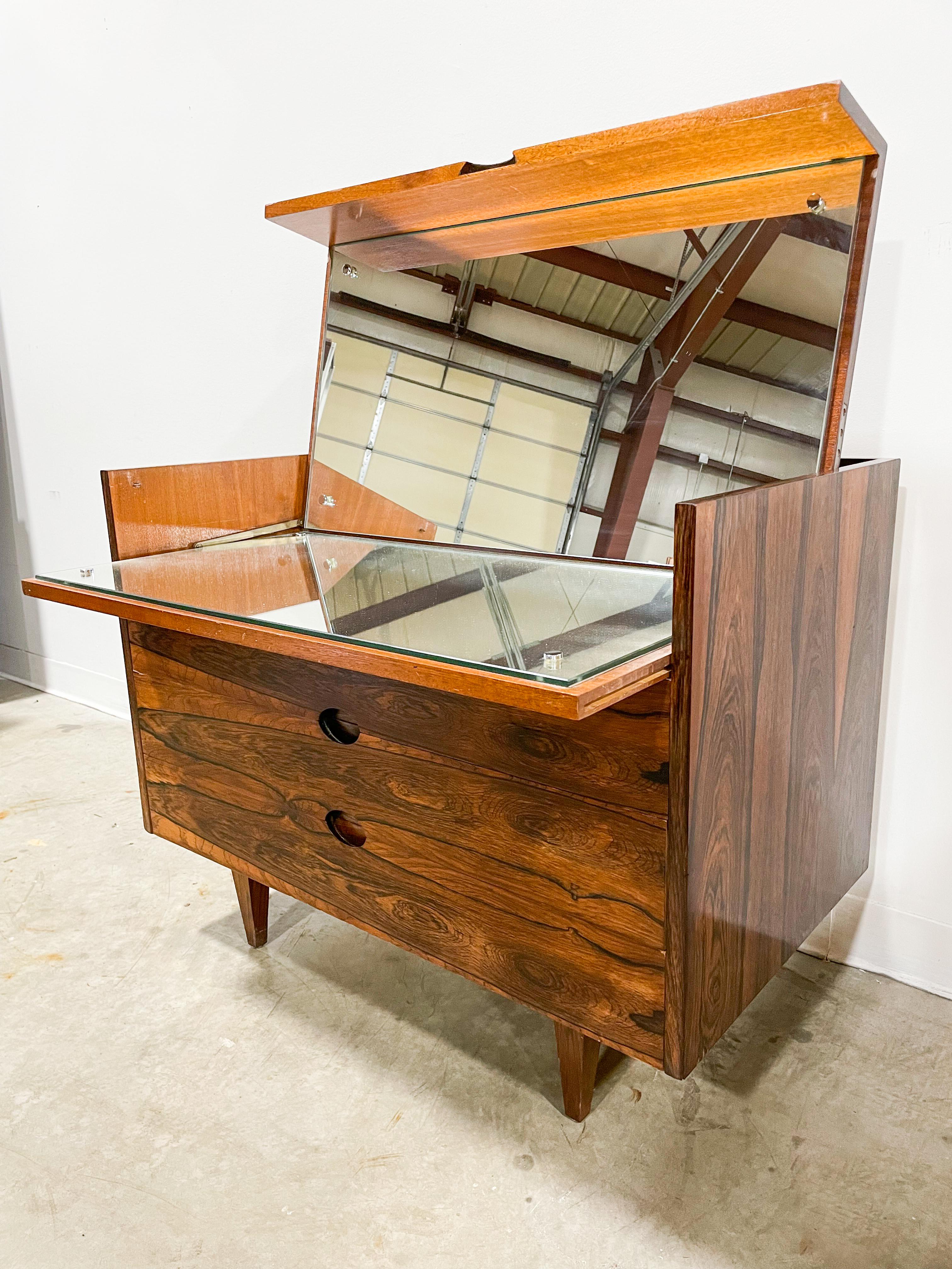In rare rosewood, this Mid-Century Modern mirrored dresser is a wonderful addition to any home. The stunning grain is eye-catching and unique, and the dresser is in very good vintage condition. The top opens up to reveal both a vertical mirror and a