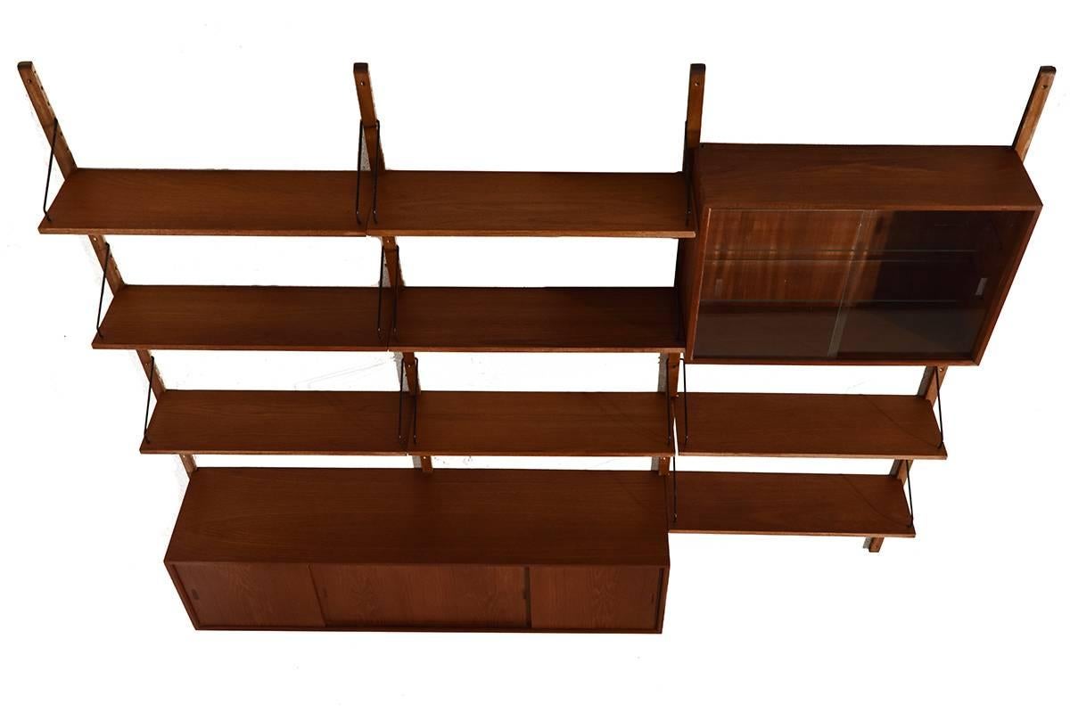 Jazzy modular wall system designed by Poul Cadovius for Royal System, Denmark in the 1960s. Timeless Danish design made in teak. 

Measures: Four wall stands 202 cm 
One sideboard 160 x 38 x 43 cm
Eight shelves 80 x 24 x 2 cm
One glass doors