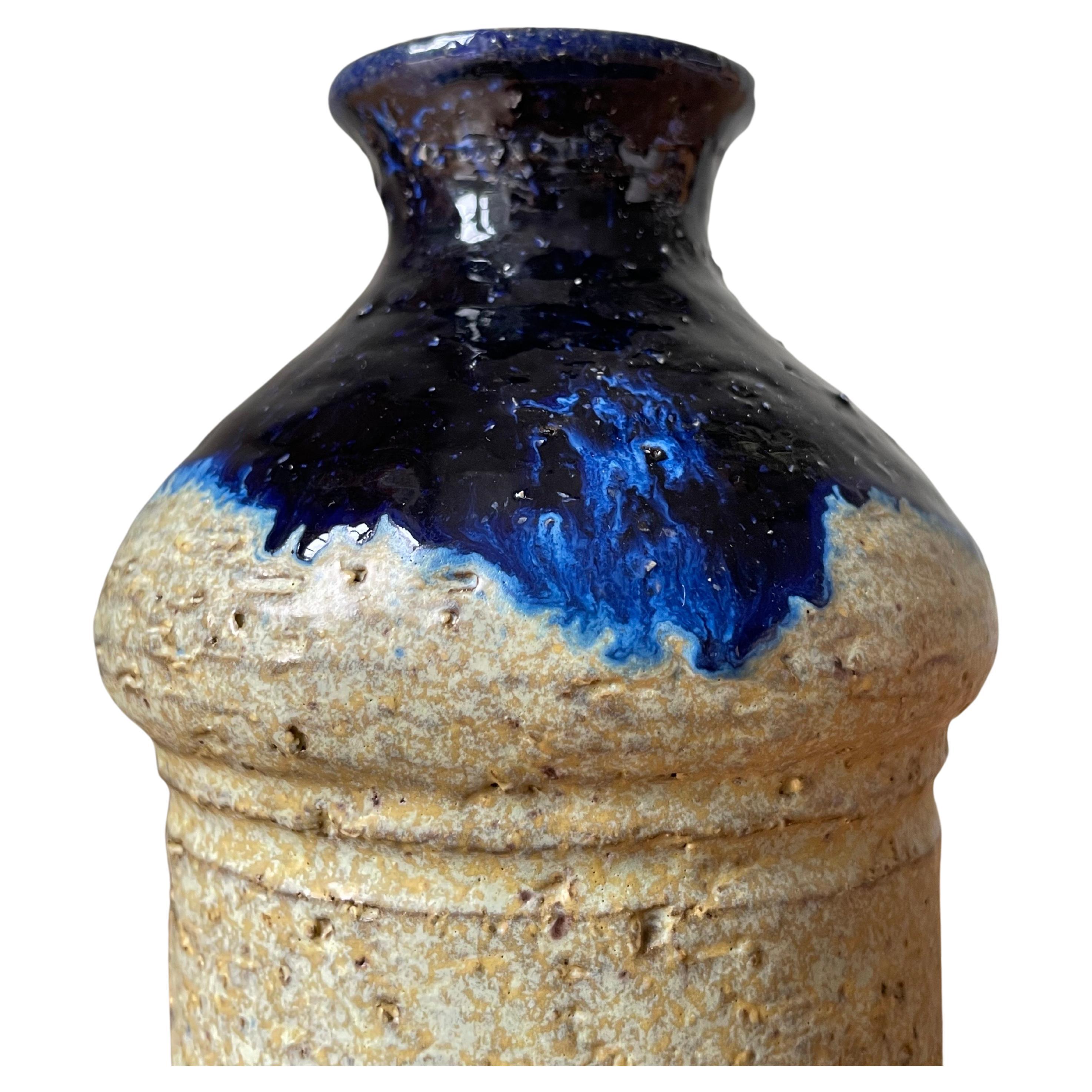 Gebogene rustikale Keramikvase mit sandfarbenem, zylinderförmigem Körper. Die abgerundete Oberseite ist mit einer glänzenden dunkelblauen Laufglasur versehen, während die Unterseite roh und unglasiert ist. Hergestellt in Dänemark in den 1960er