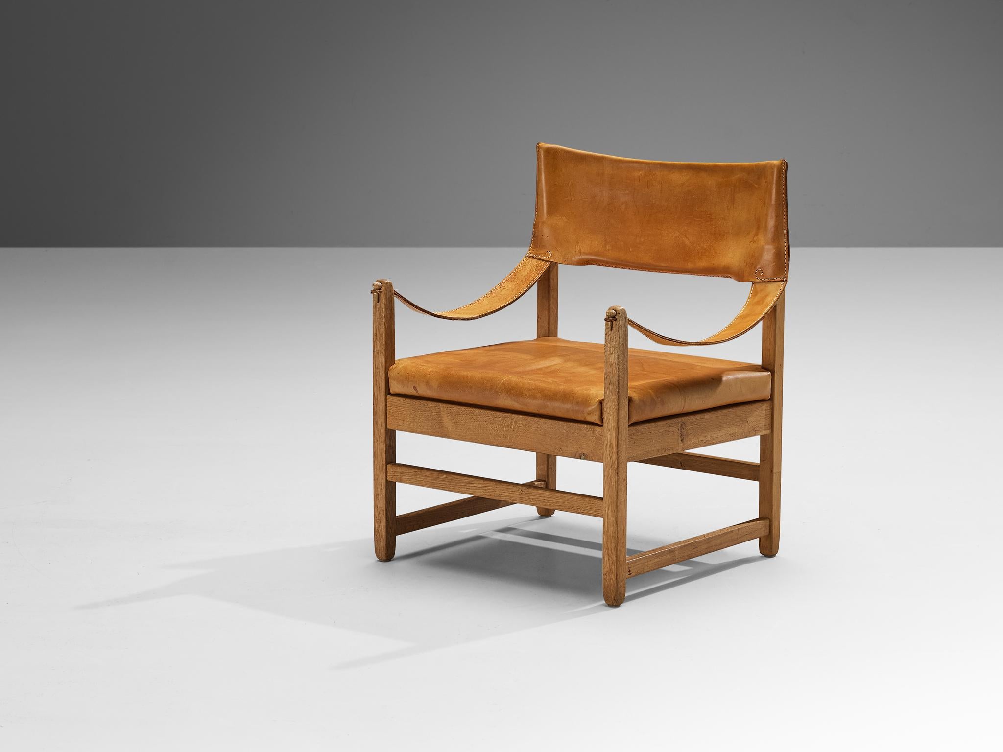 Armchair, leather, oak, Denmark, 1960s

Well-constructed armchair from Denmark with a solid appearance. Sculpted wooden elements constitute its framework. As characteristic for safari chairs, the armrests are made of thick straps that are