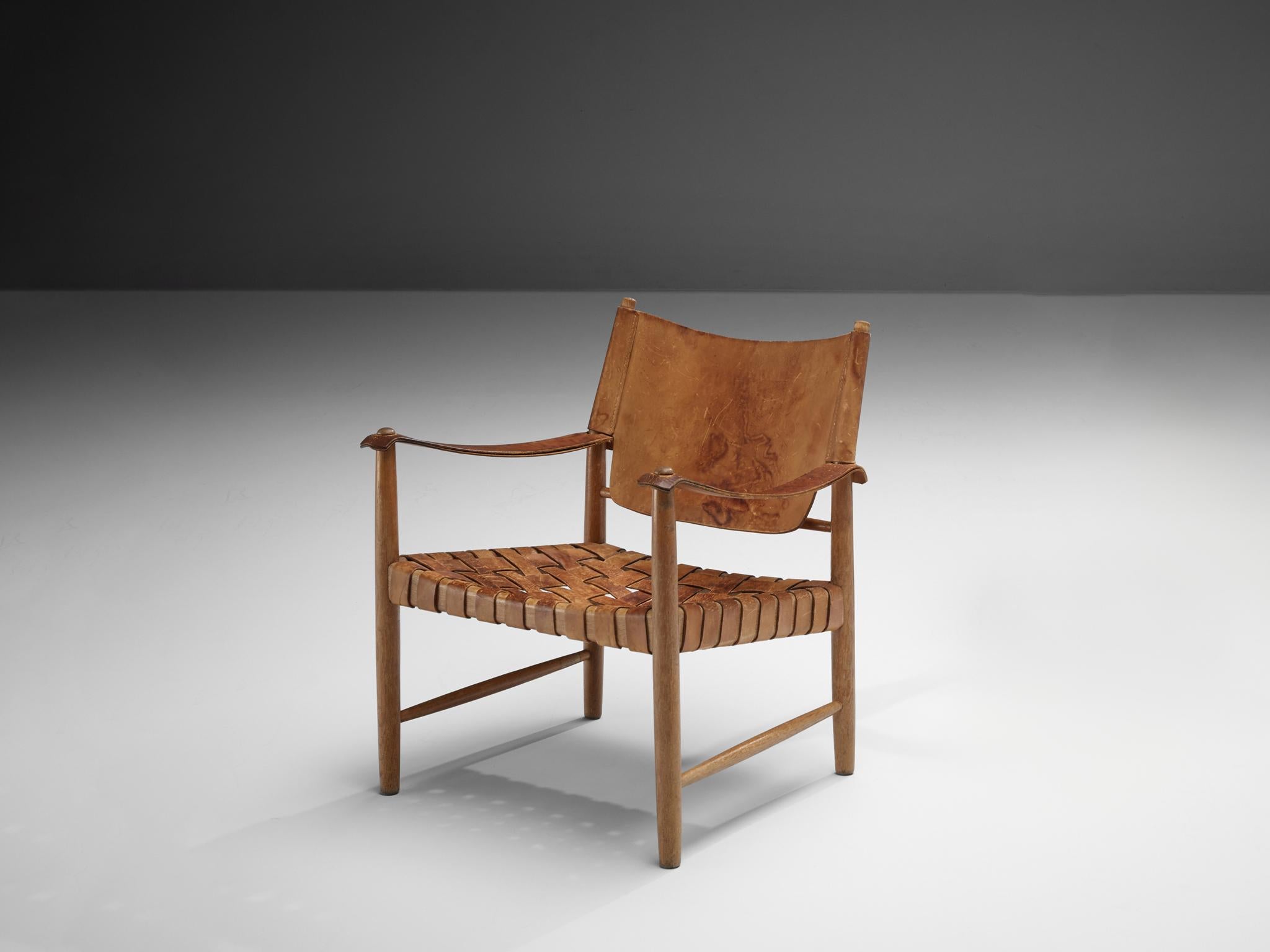 Safari chair, patinated leather, oak, Denmark, 1950s. 

This elegant safari chair features wonderful patinated leather on both the seat, the arms and back. The patina creates a lively and lived-in character that is achieved because years and years