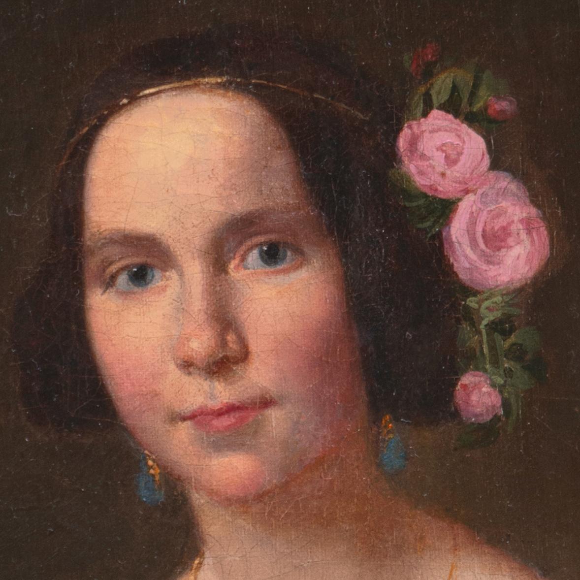 A delicately-observed, three-quarter length oil portrait of a young woman in society, fashionably dressed in a pinch-waisted, embroidered chiffon ball-gown and wearing a gold pendant and teardrop earrings with tea roses in her hair; the subject