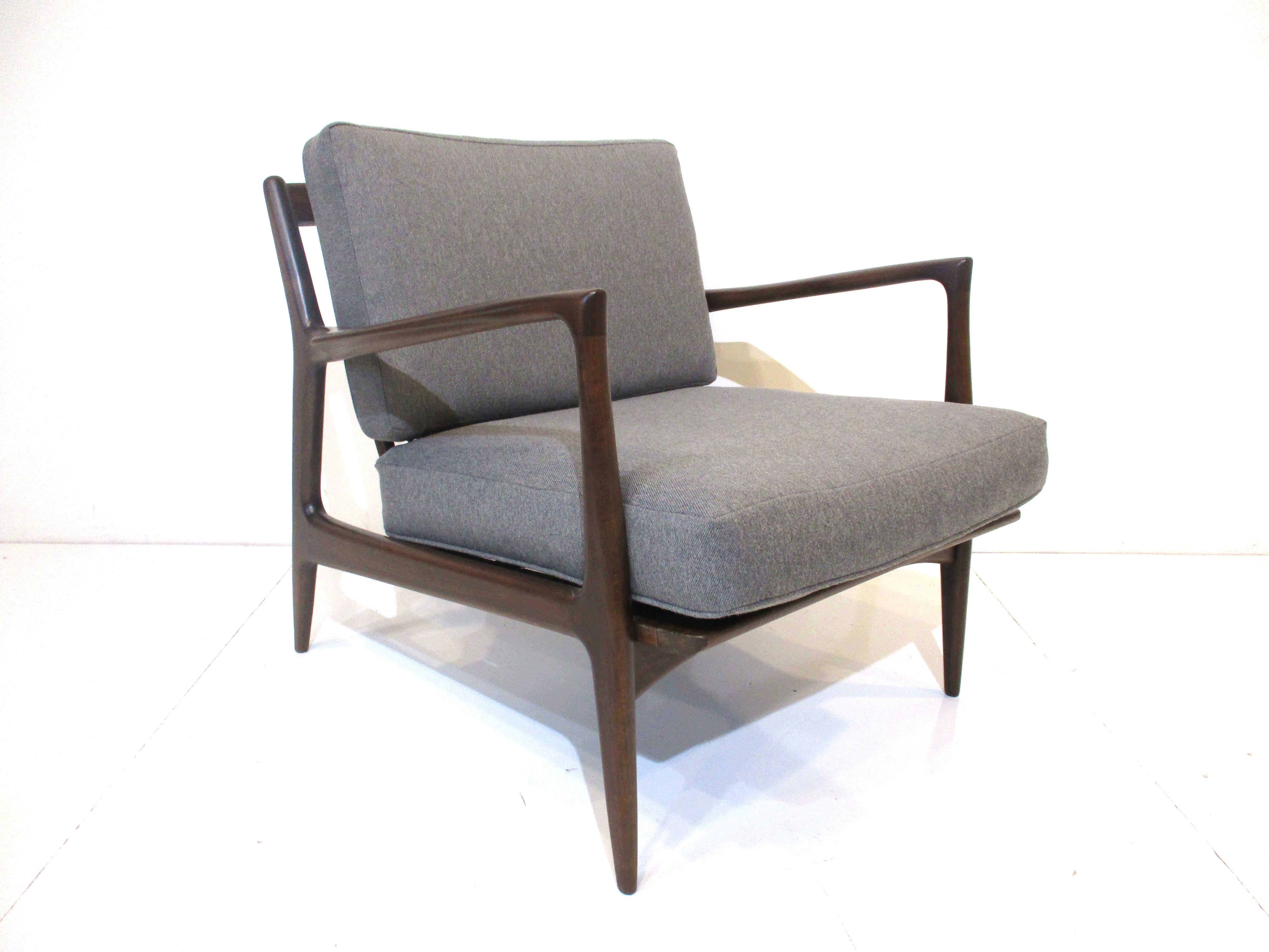 A dark walnut toned sculptural wood framed lounge chair with two loose upholstered cushions in a nice warm gray woven fabric . Designed by Ib Kofod Larsen made in Denmark and imported by the Selig furniture company . Very well crafted , designed and