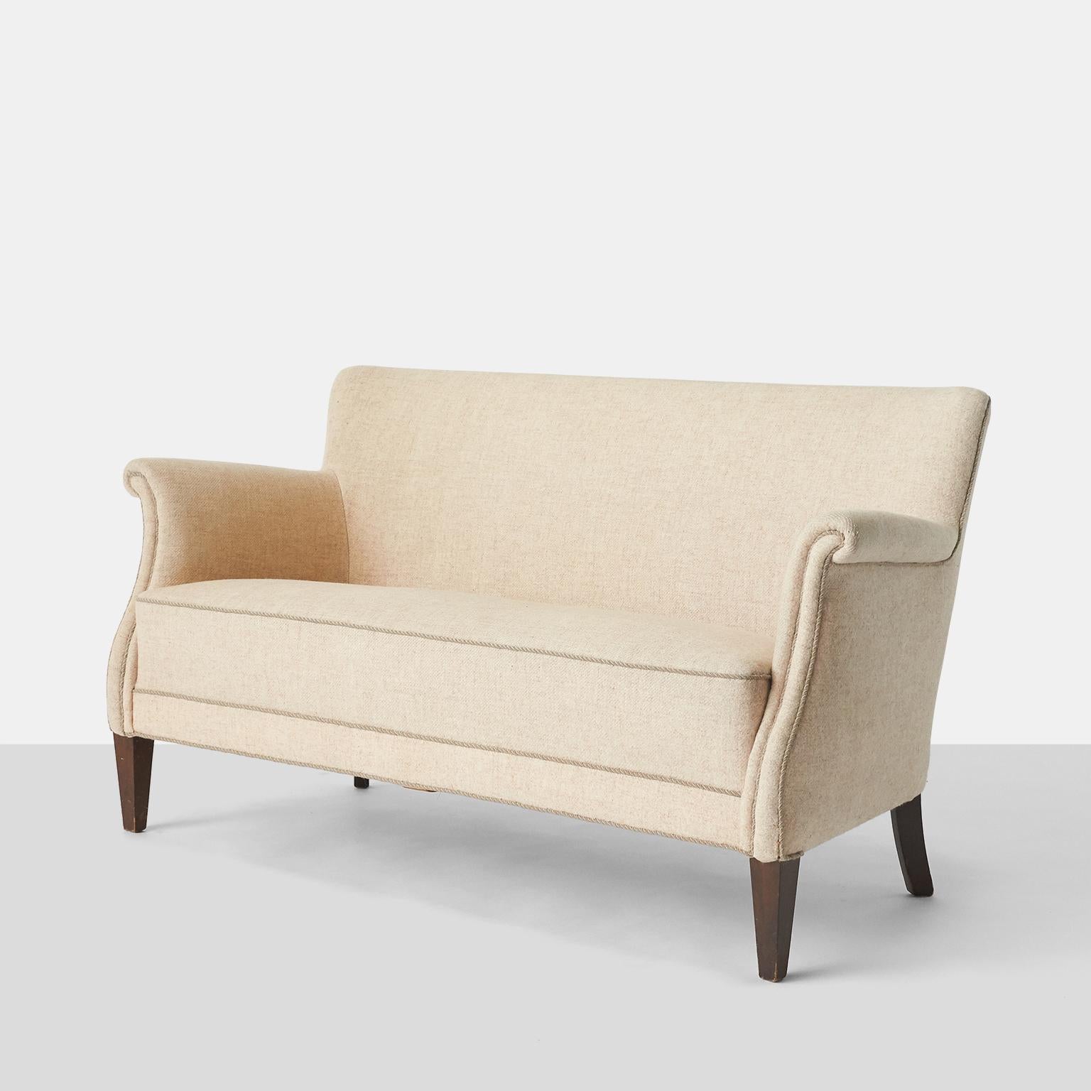 A Danish settee upholstered in beige linen, with piping along all the edges, including the rolled arms, and mahogany legs. 

Seat has eight-way hand tied springs in excellent condition. The frame is firm and stout. Needs to be reupholstered.