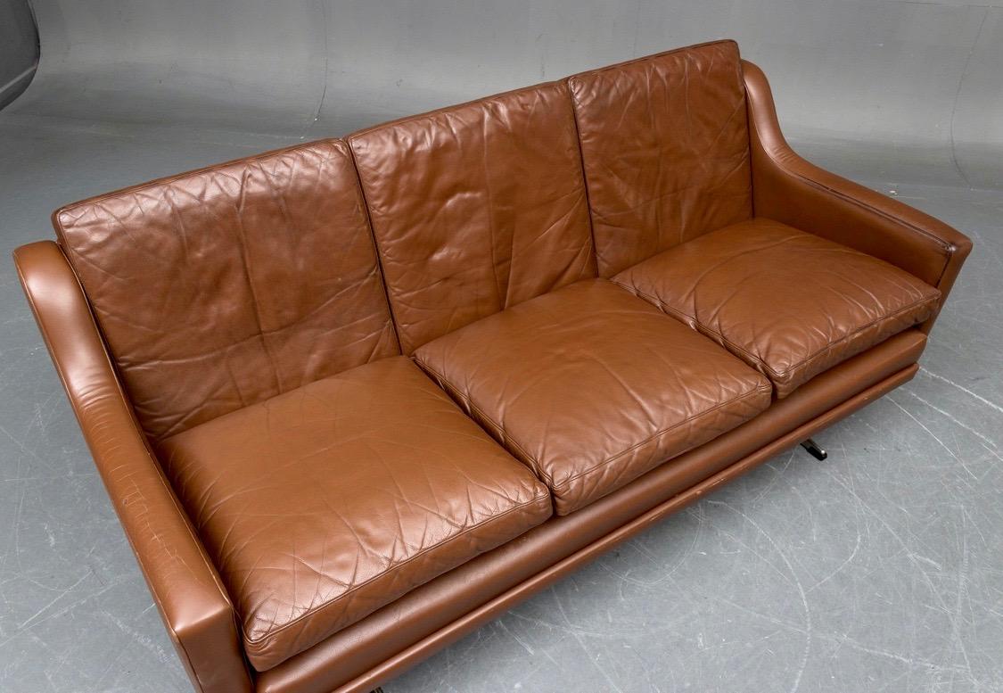 Danish midcentury three-seat sofa with removable cushions on chromed shaker steel frame, covered with brown leather L. 175 cm. H. 70 cm. Seat height: 45 cm. Traces of wear and patina of the leather.